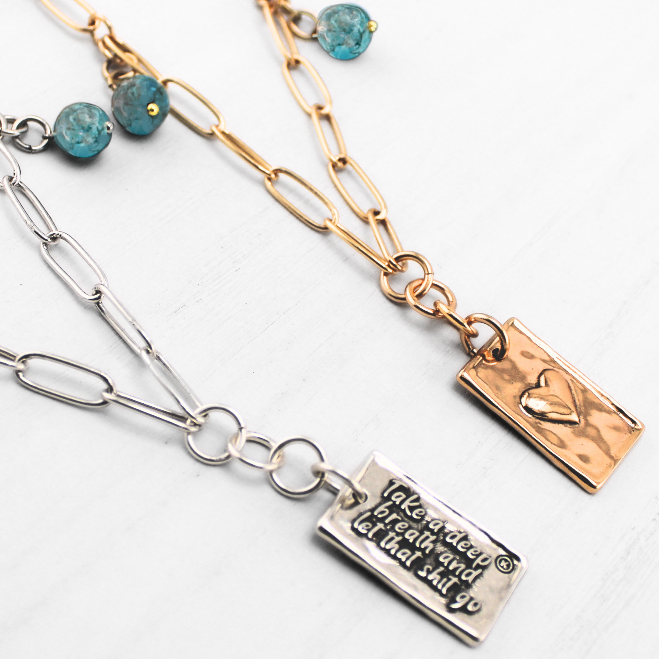 A brass necklace with a paperclip chain design, featuring a rectangular pendant with a heart cut-out and two magnesite accent stones on a white background.