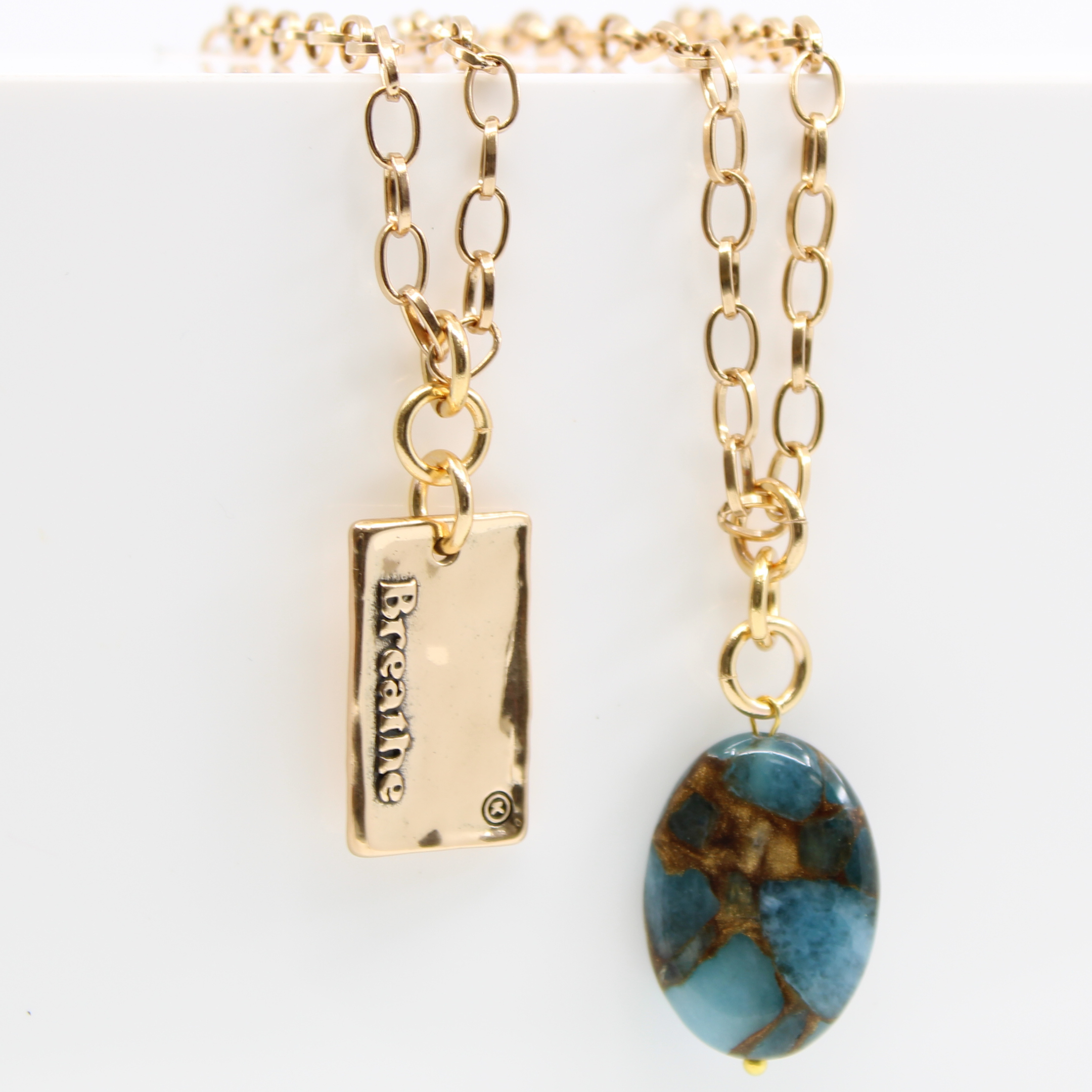 A person wearing a denim shirt and a white lace top, showcasing a silver-colored stainless steel chain necklace with a square pendant.