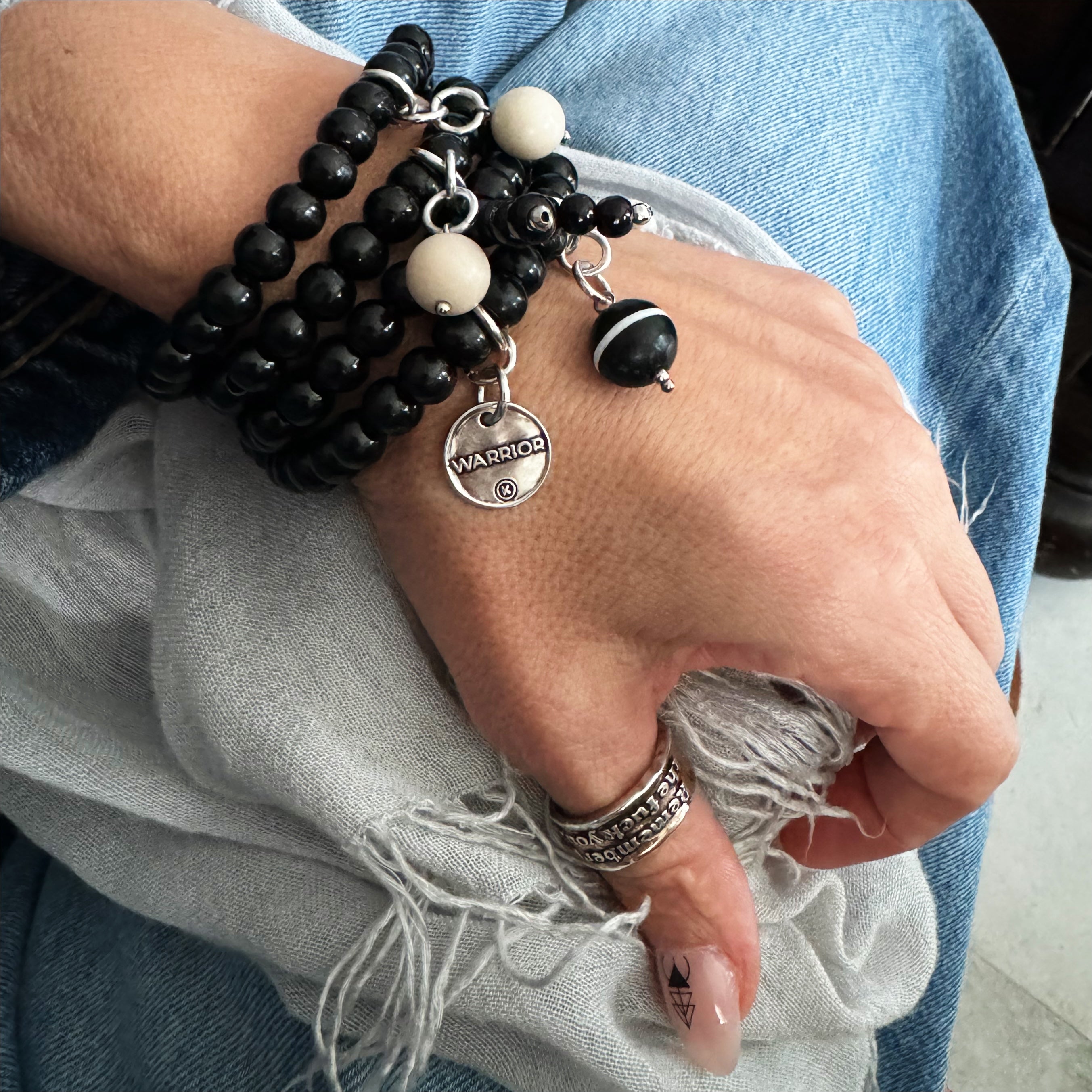 A person's wrist wearing a black wooden Boho wrap bracelet with a silver finish pendant and river stone accents.