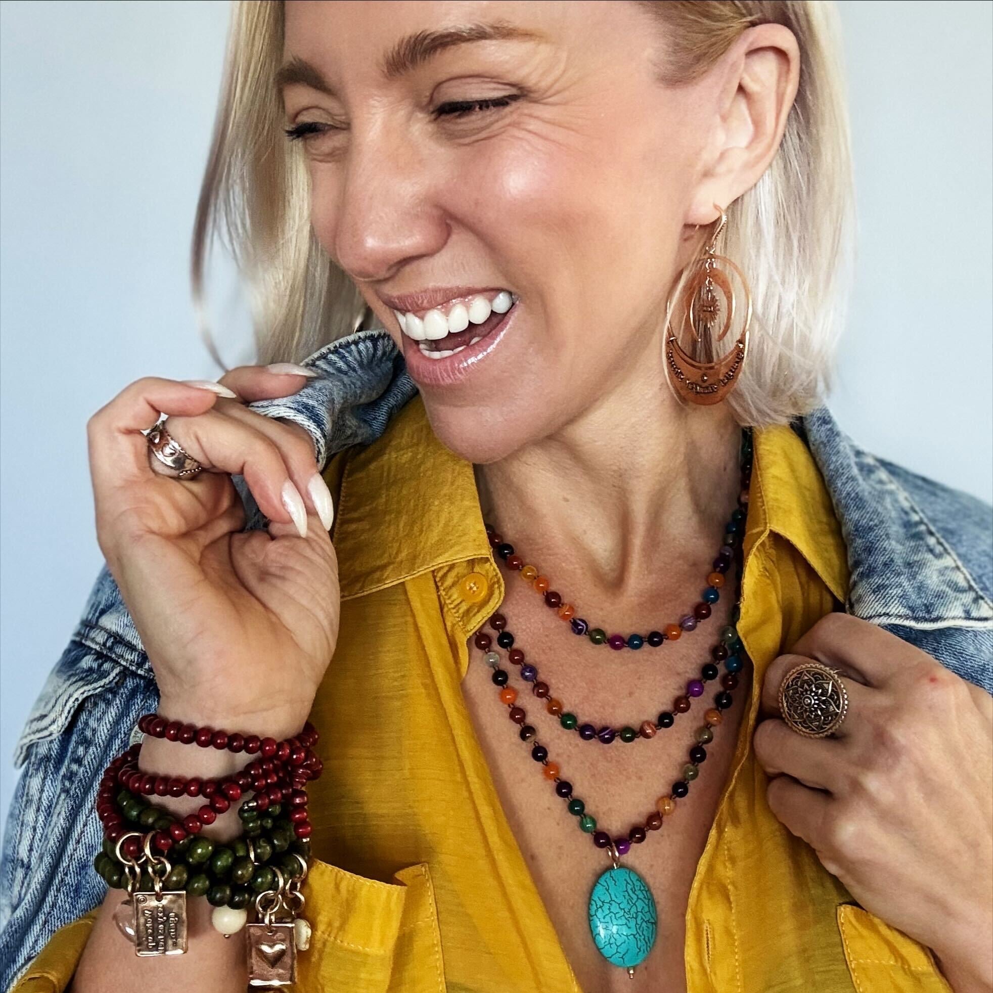 Woman wearing a yellow shirt, colorful jewelry, and a denim jacket against a light blue background