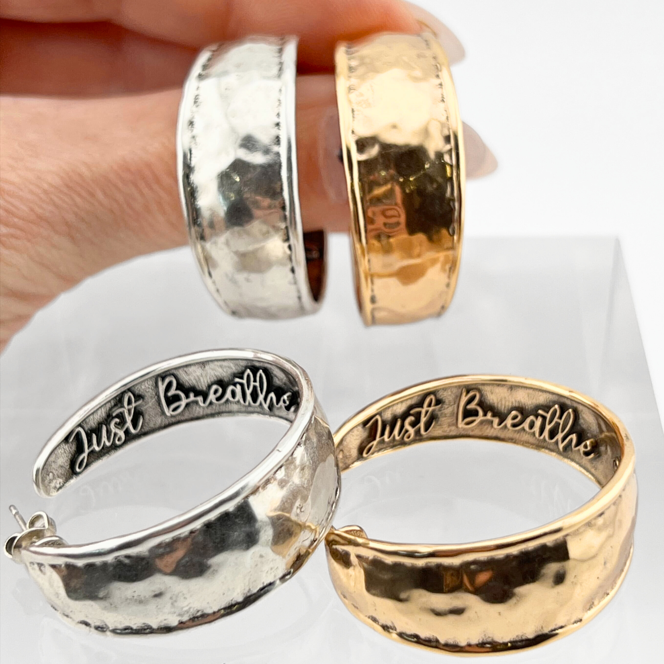 A pair of hoop earrings with a hammered texture in silver and gold colors, featuring the inscription 'JUST BREATHE' on the silver earrings, and 'I JUST BREATHE' on the gold earrings.