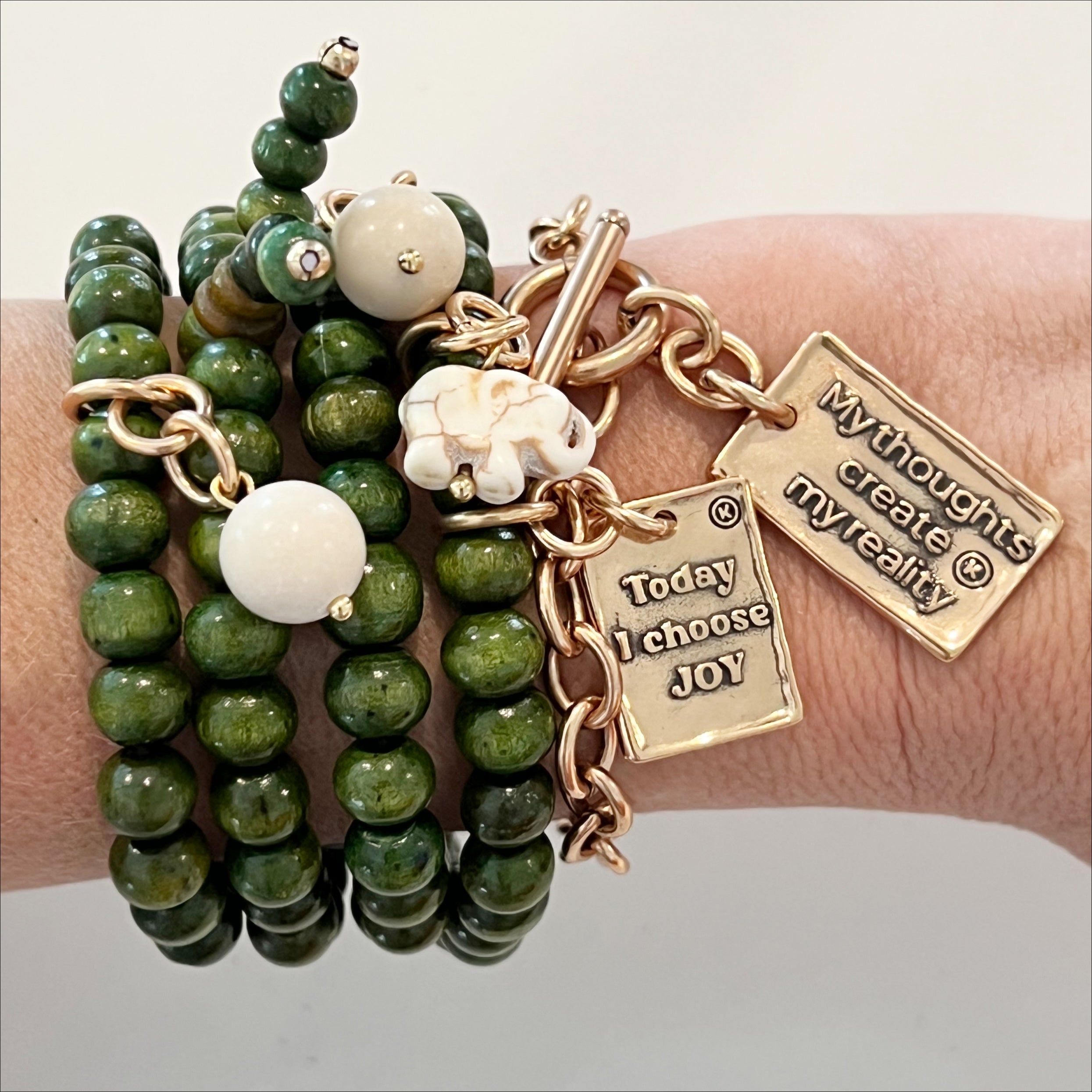 A wooden boho style bracelet with green beads, gold finish pendant, and an off-white howlite elephant charm displayed on a wrist.