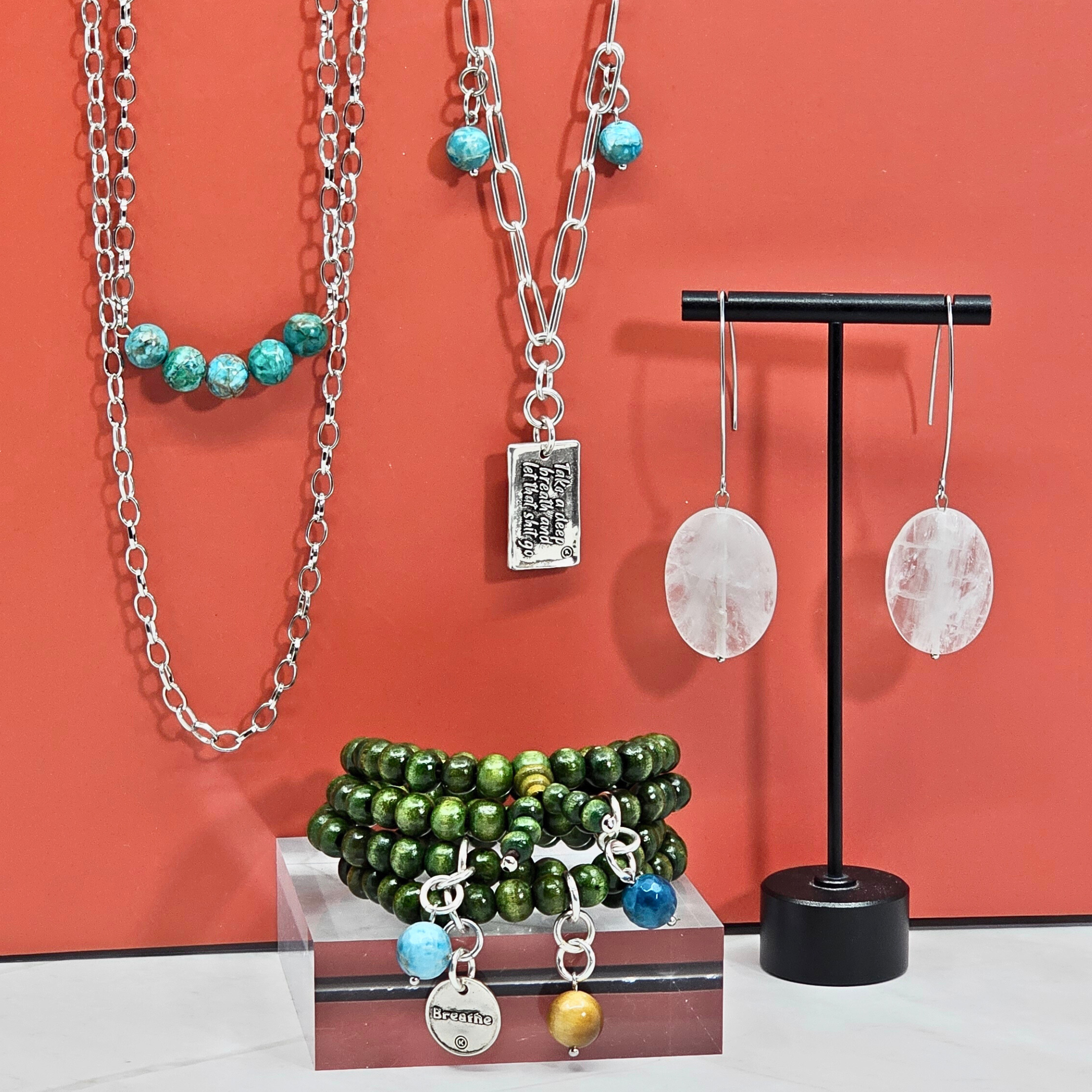 Jewelry set including necklaces, bracelets, and earrings on a stand against an orange background