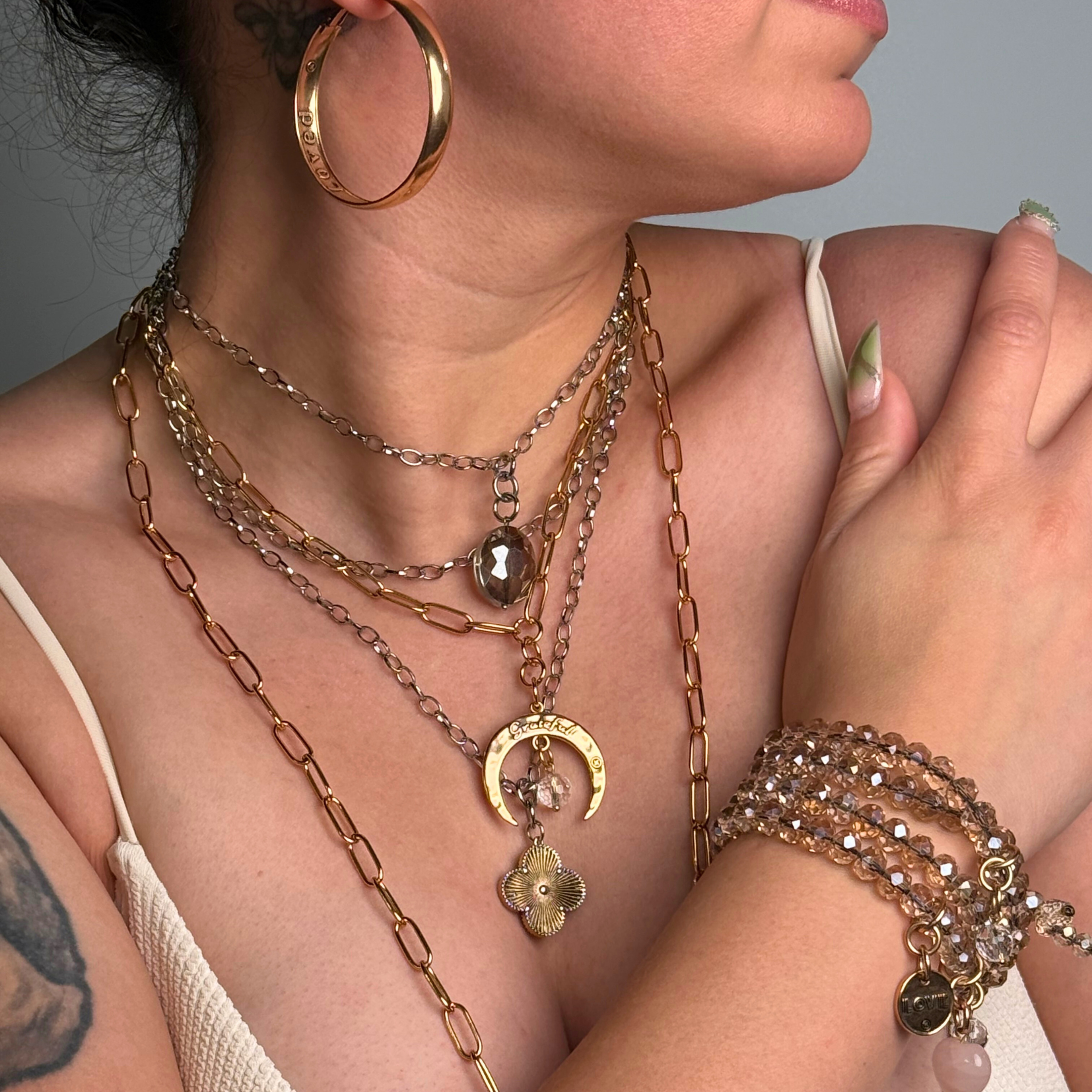 Close-up of a person wearing multiple necklaces and bracelets with a neutral background