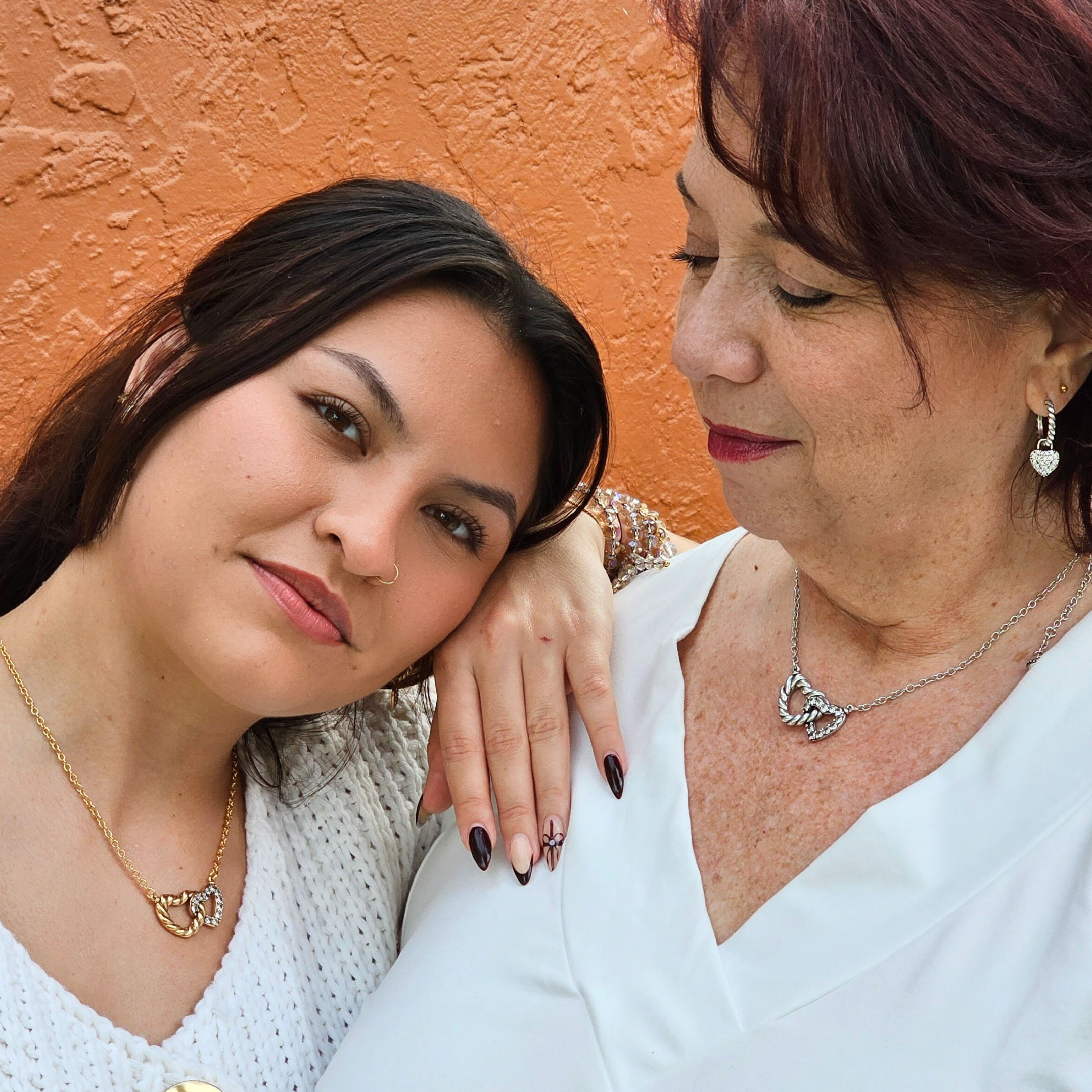 Two women posing together against an orange wall.
