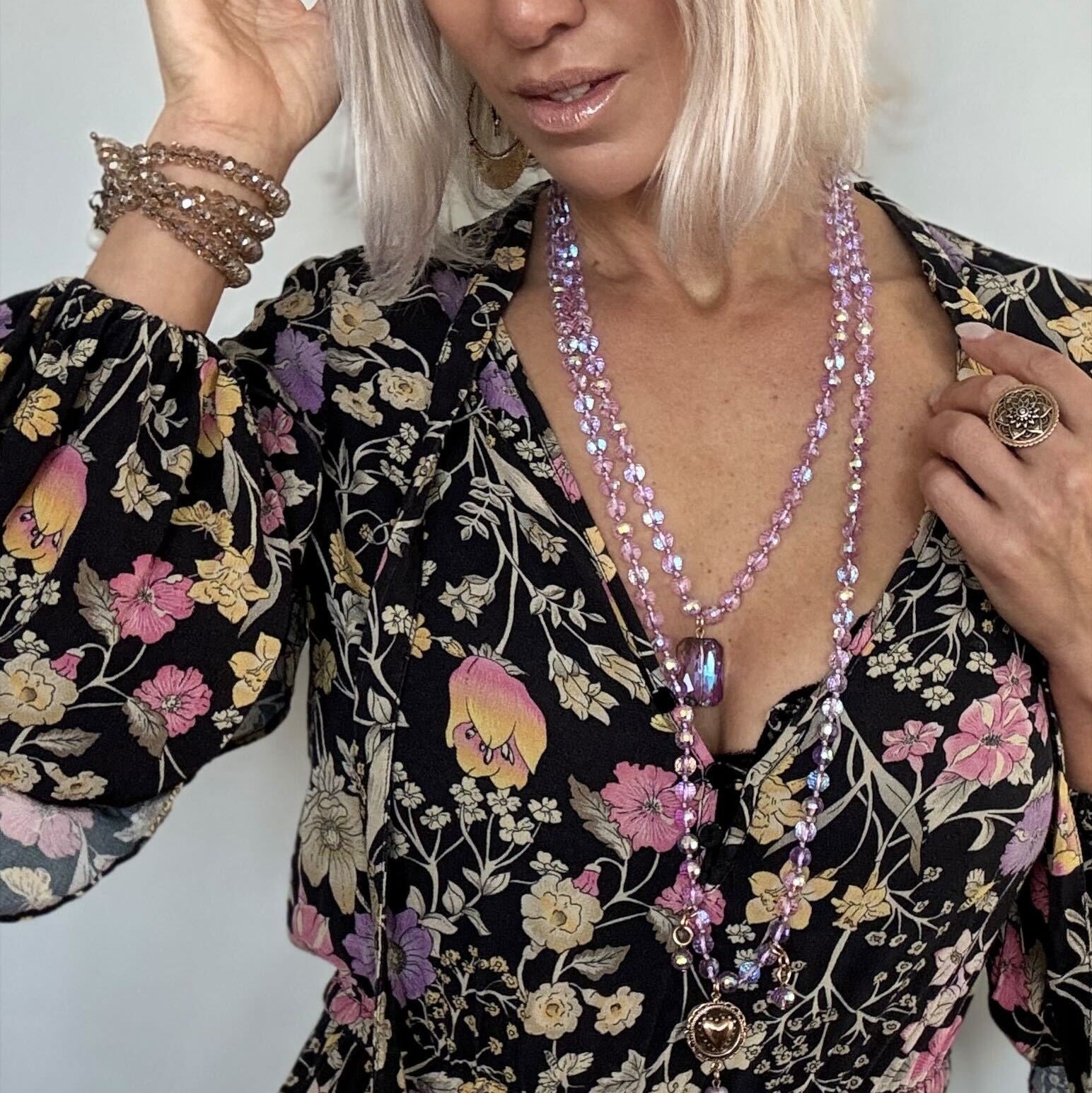 Woman wearing a floral dress and multiple necklaces with a plain background