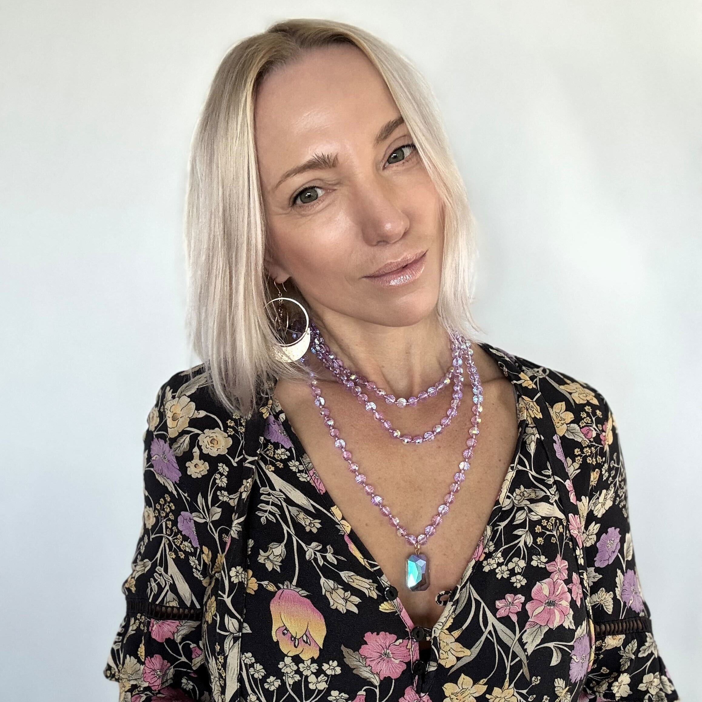 Woman wearing a floral blouse and multiple necklaces against a white background