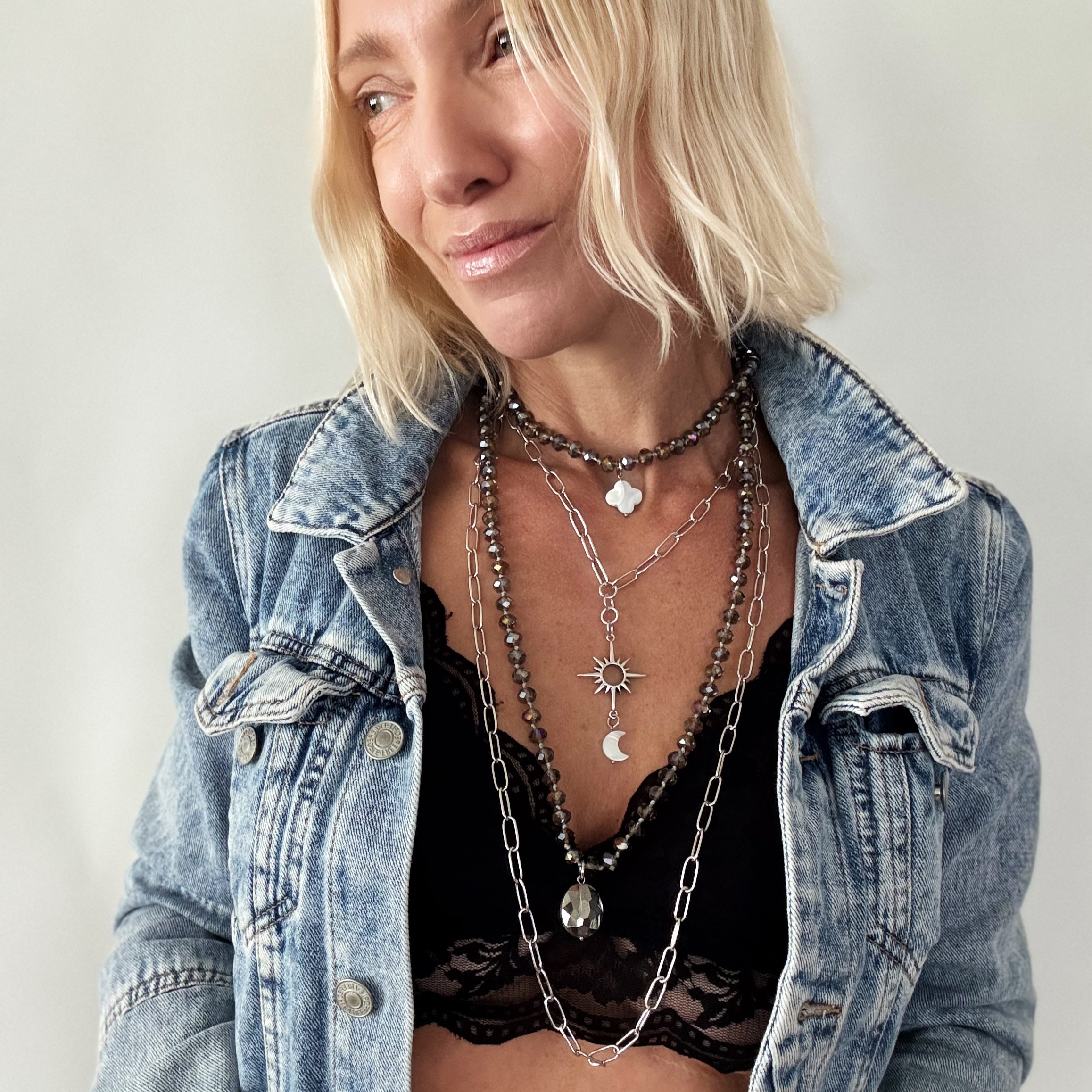 Woman wearing a denim jacket and layered necklaces against a plain background