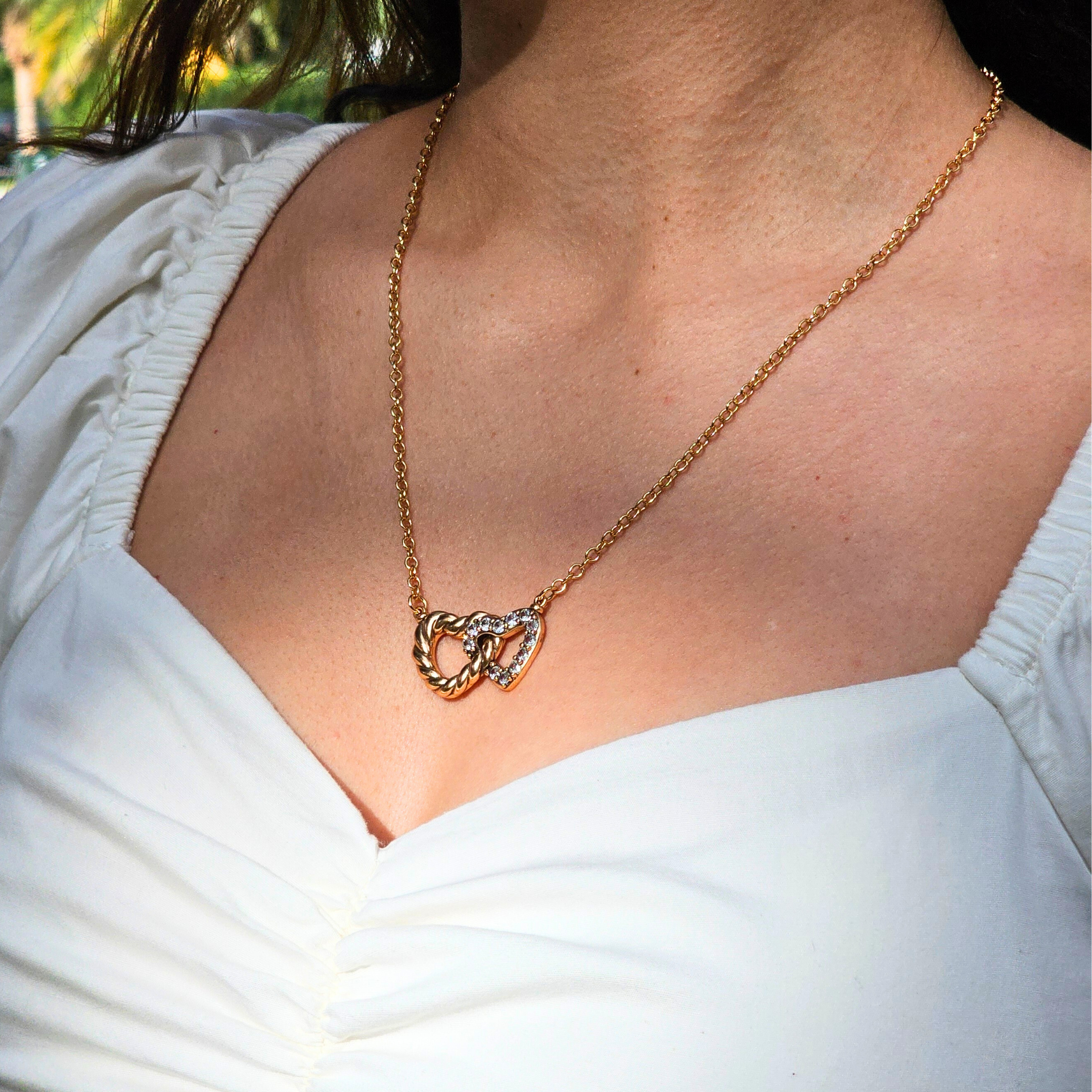Gold necklace with a heart-shaped pendant worn by a person in a white top.