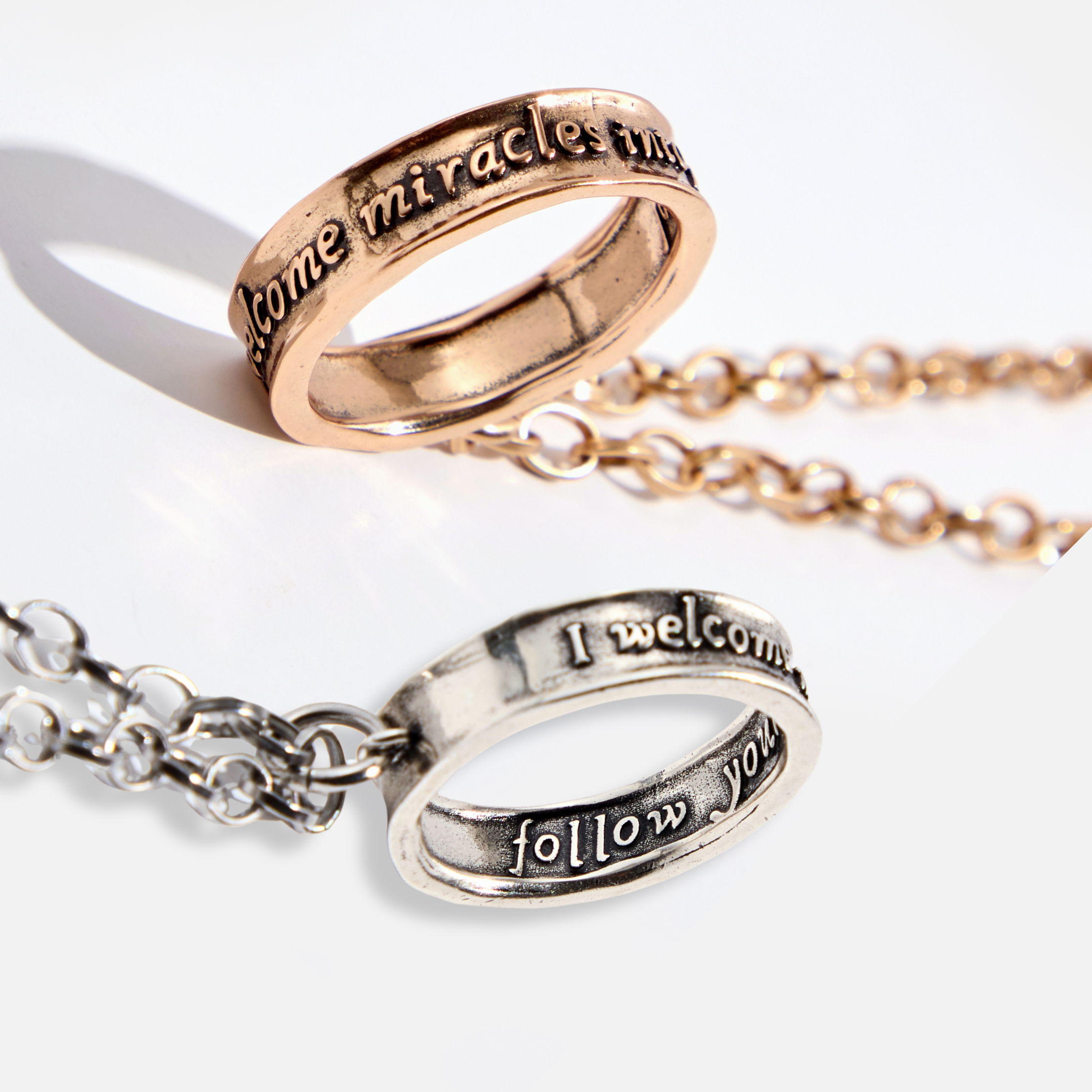 A collection of stainless steel jewelry, featuring a necklace with a gold chain and a matching ring with an inscription, alongside a silver chain necklace with a different inscription.