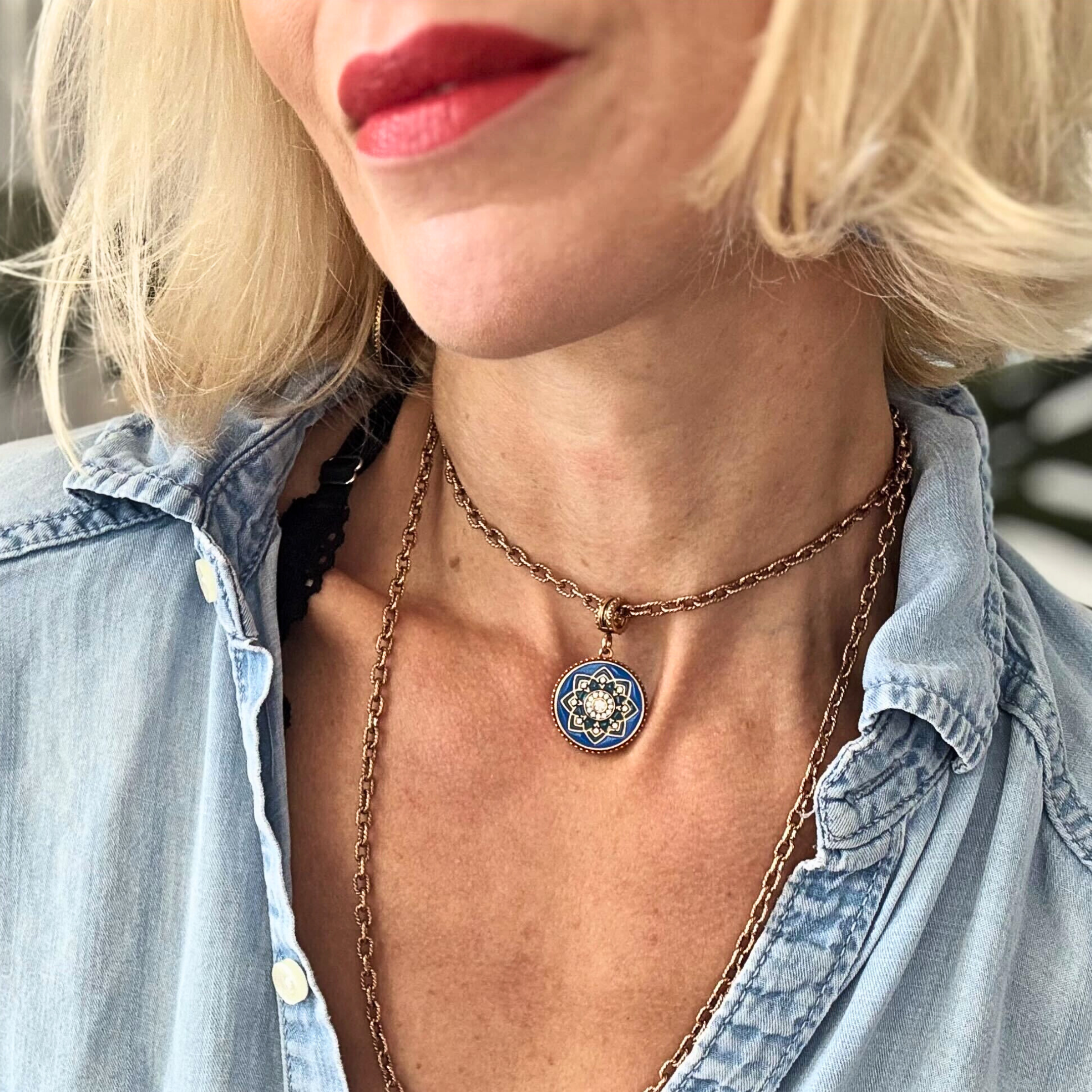 Close-up of a person wearing a necklace with a blue pendant, wearing a denim shirt.