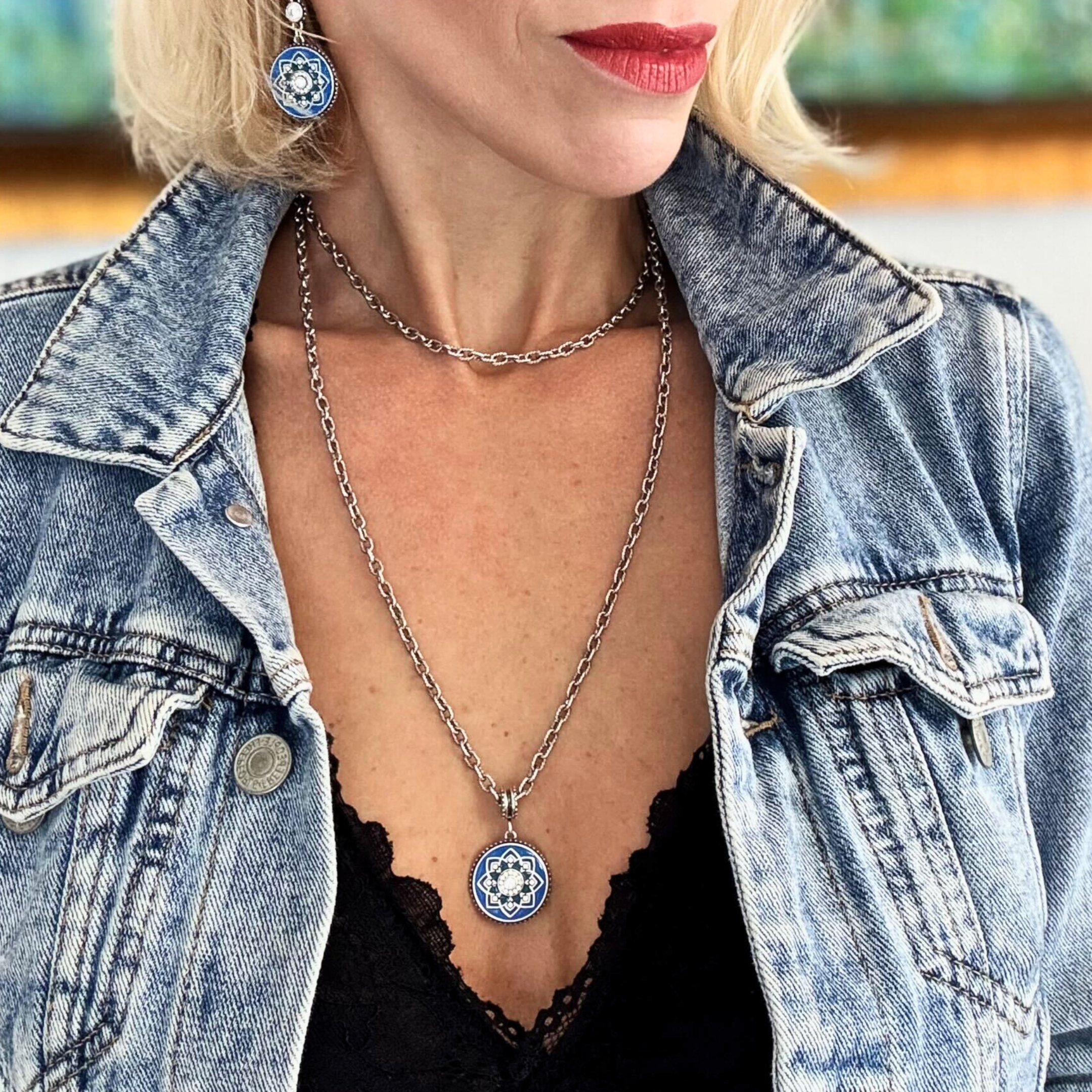 Person wearing a denim jacket with a necklace and earrings, blurred background