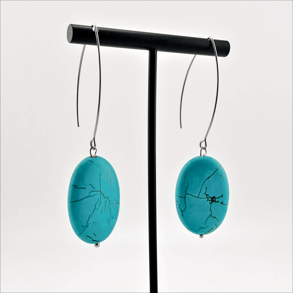A person wearing large stone drop earrings with a V-shape wire earring holder.