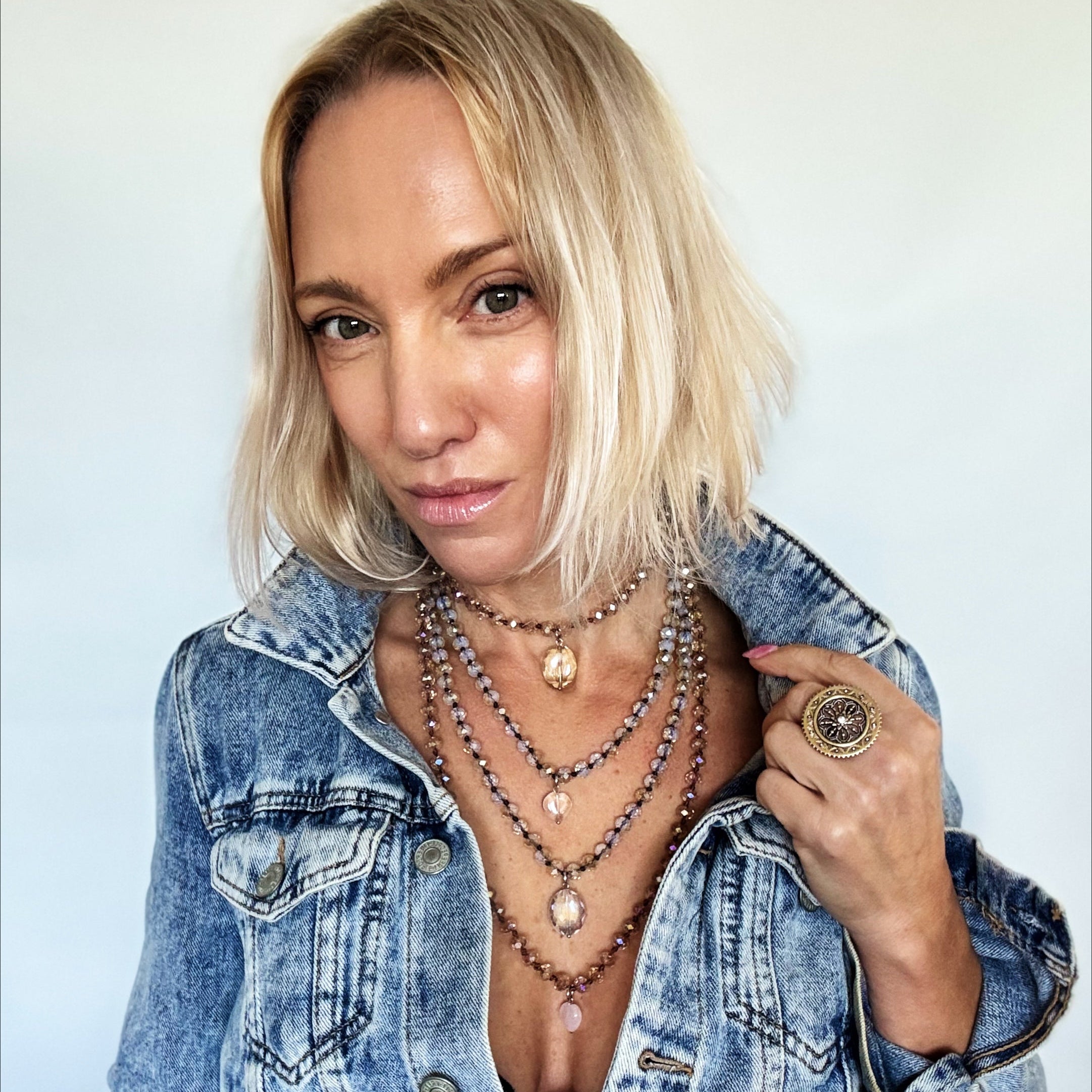 Woman wearing a denim jacket with layered necklaces against a plain background