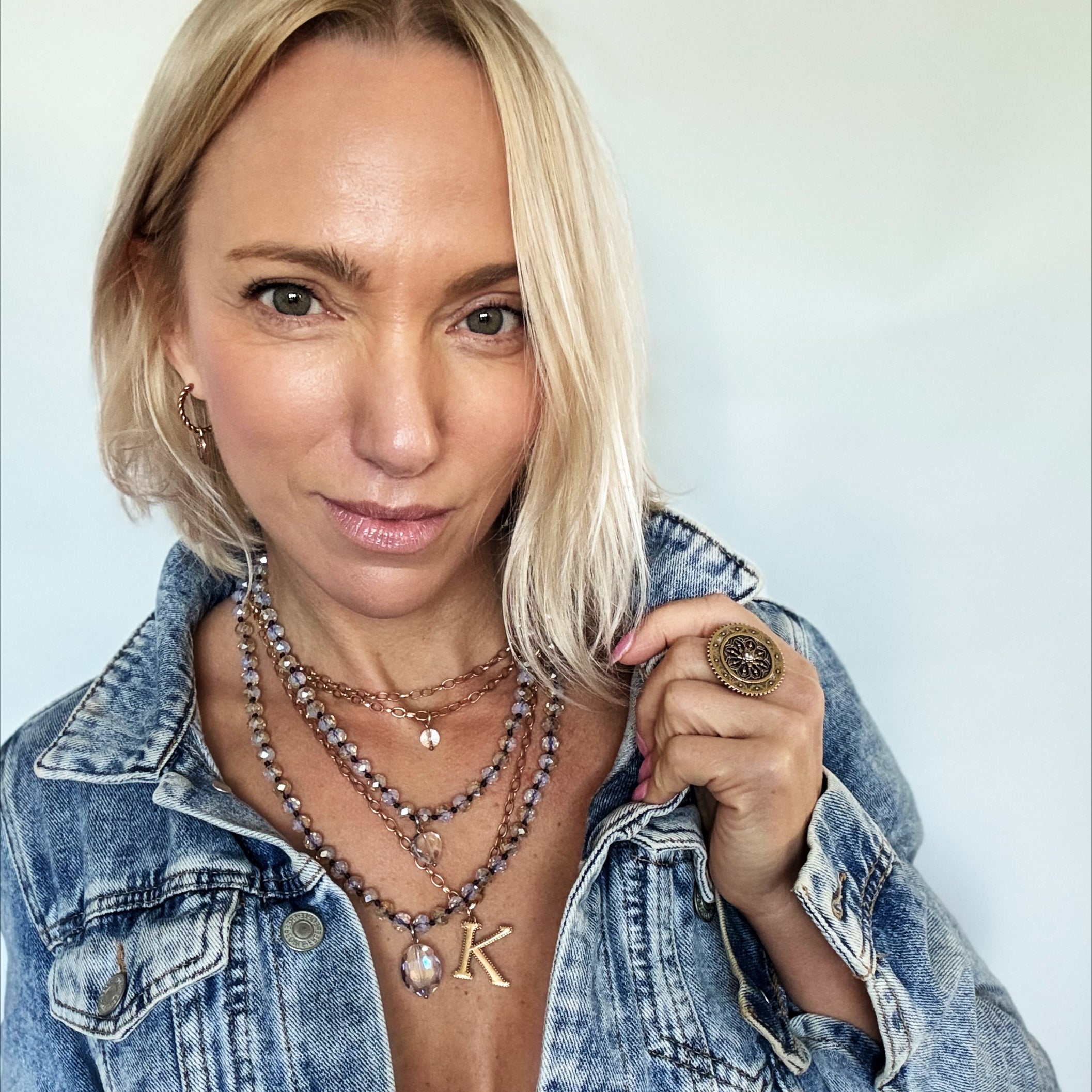 Woman wearing a denim jacket with layered necklaces and a key-shaped pendant.