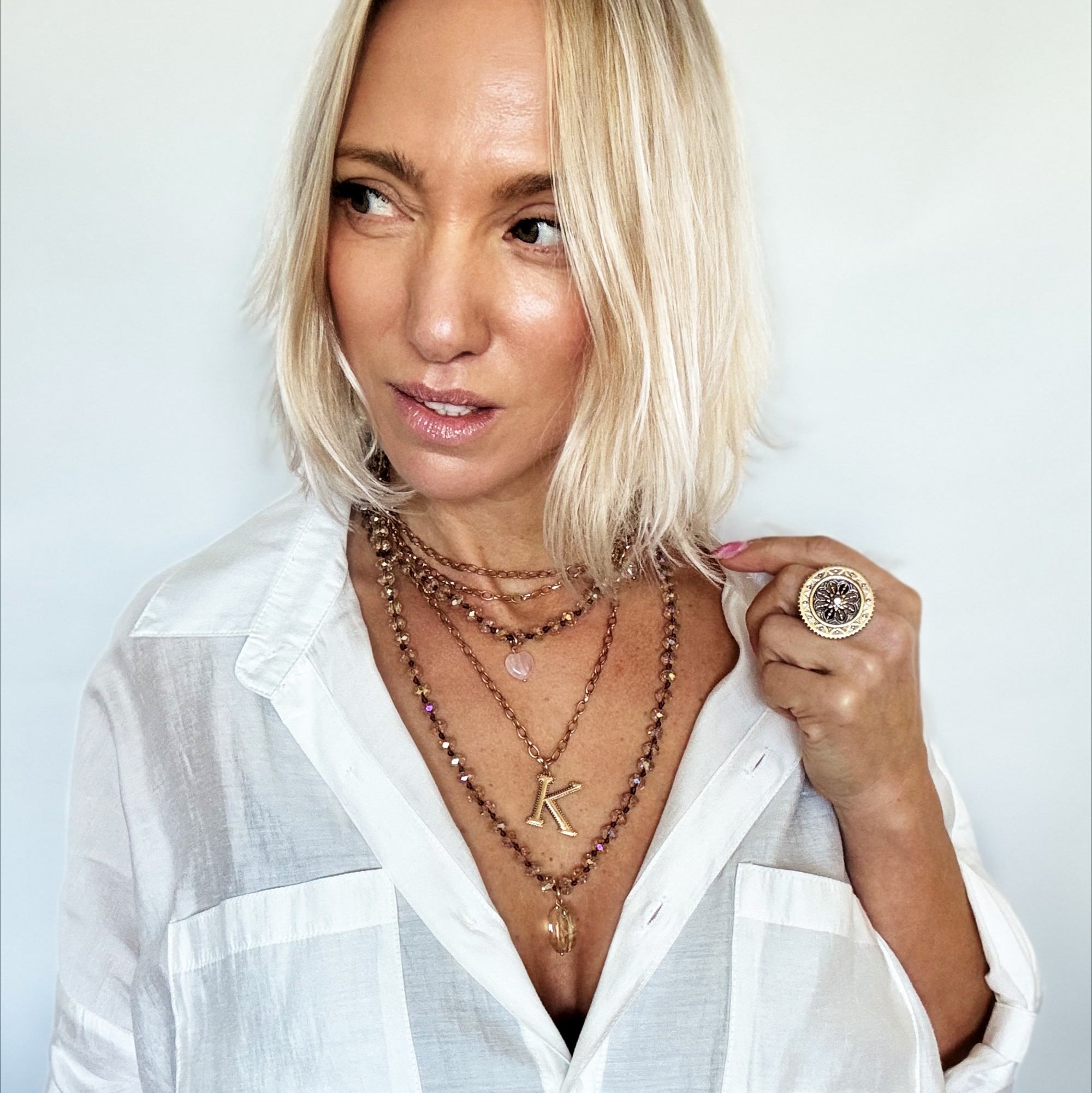 Woman wearing multiple necklaces and a ring against a plain background