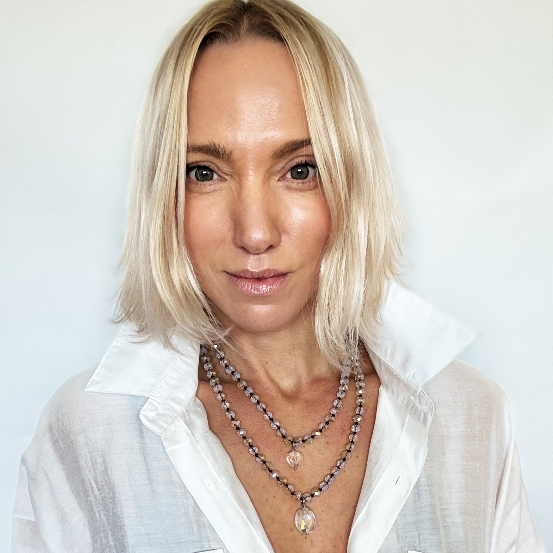 Woman wearing a white shirt and multiple necklaces against a light background