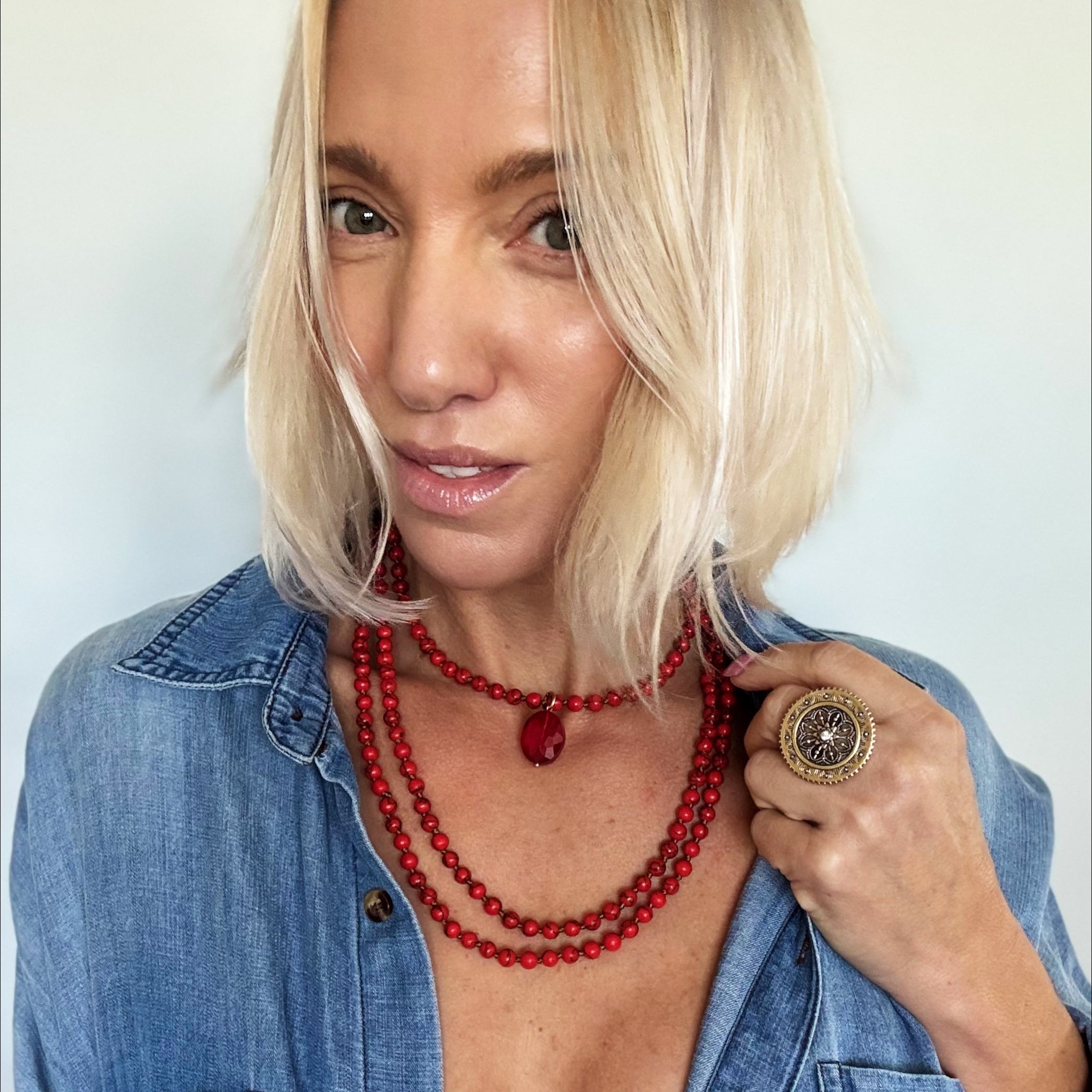 Woman wearing a blue denim shirt and red beaded necklace with a plain background