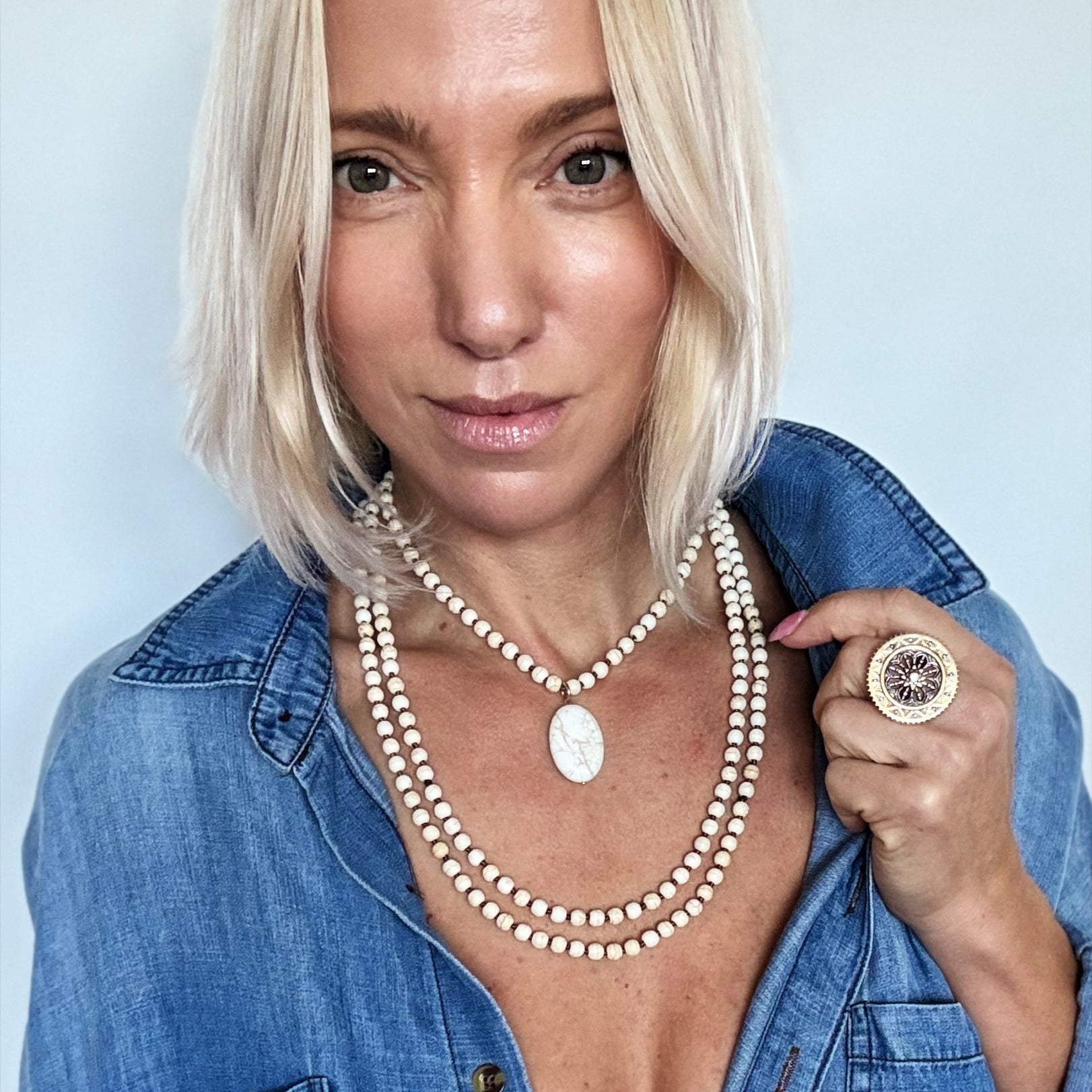 Woman wearing multiple pearl necklaces and a denim jacket against a light blue background