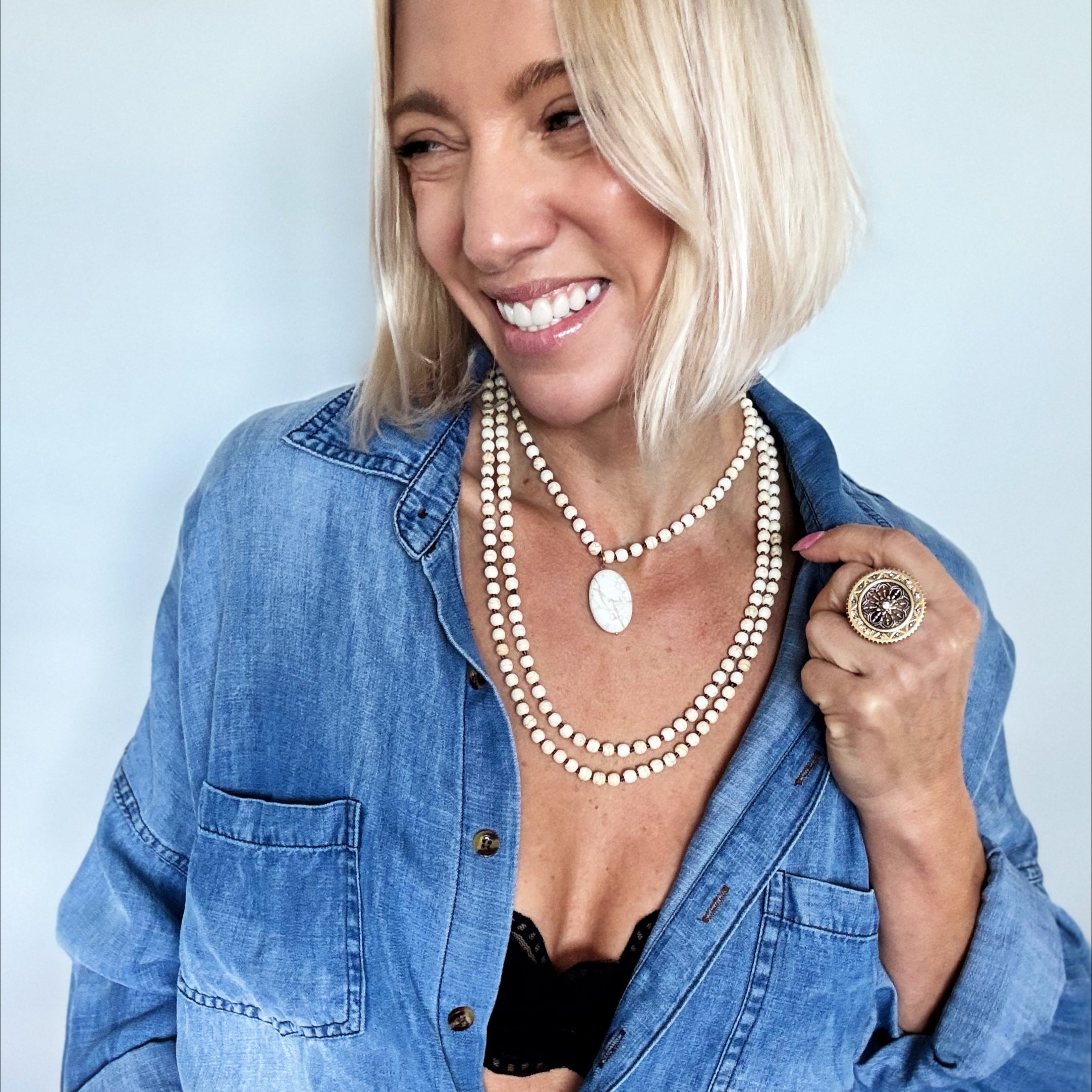 Woman wearing a blue denim shirt with an open collar, revealing a black bralette, against a light blue background.
