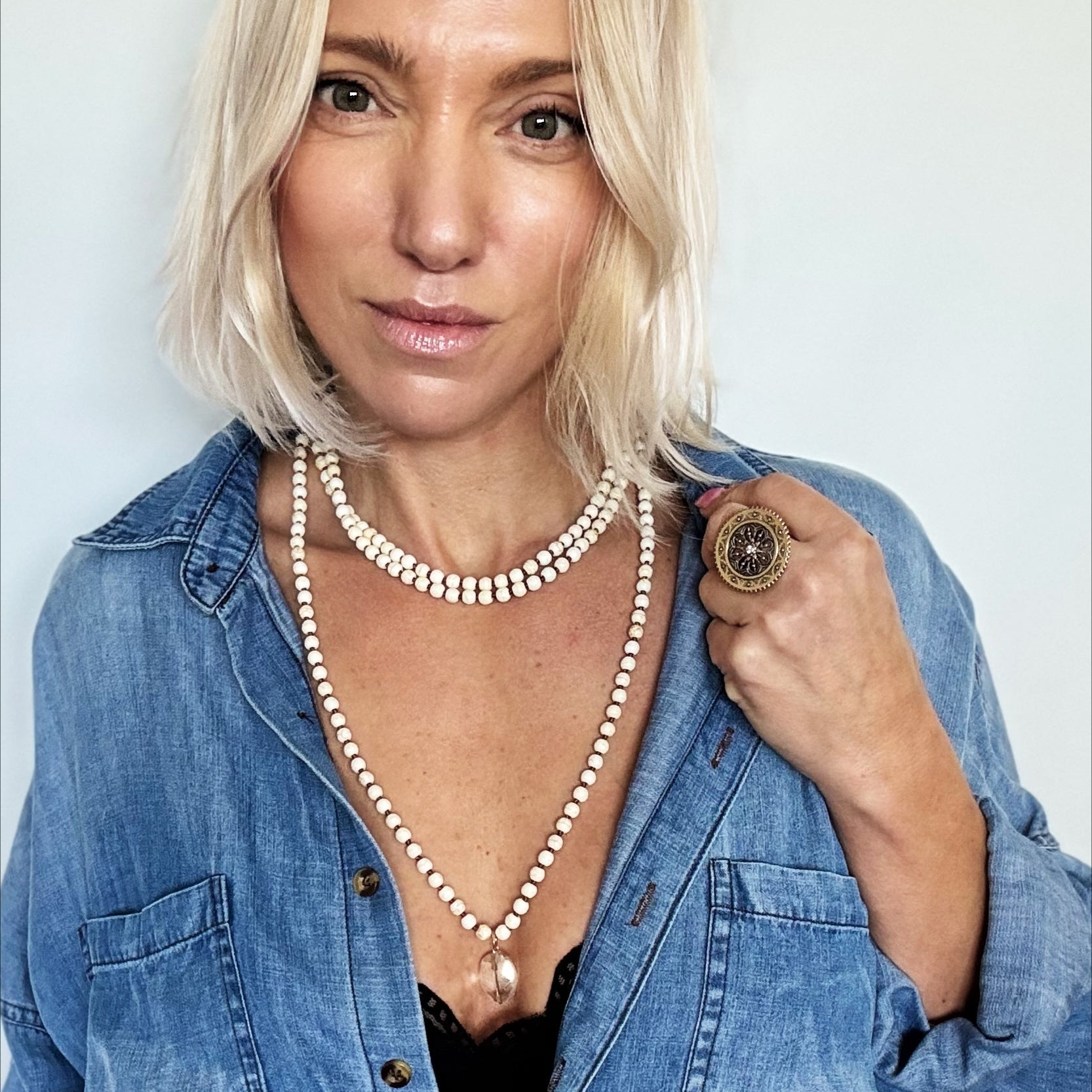 Woman wearing a blue denim shirt and pearl necklace against a plain background