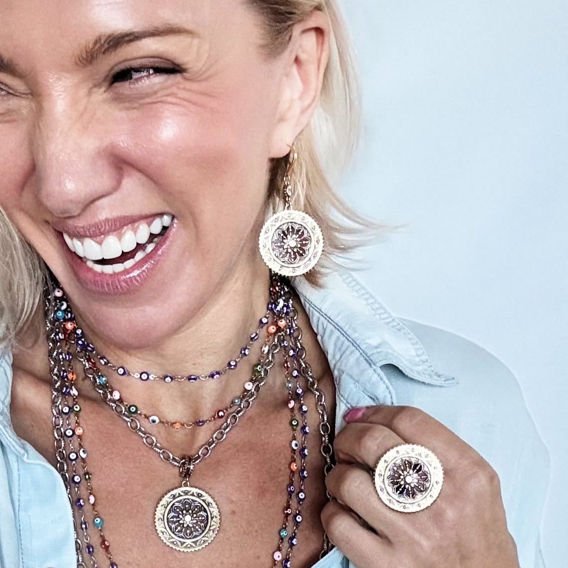 Woman wearing layered necklaces and earrings against a light blue background