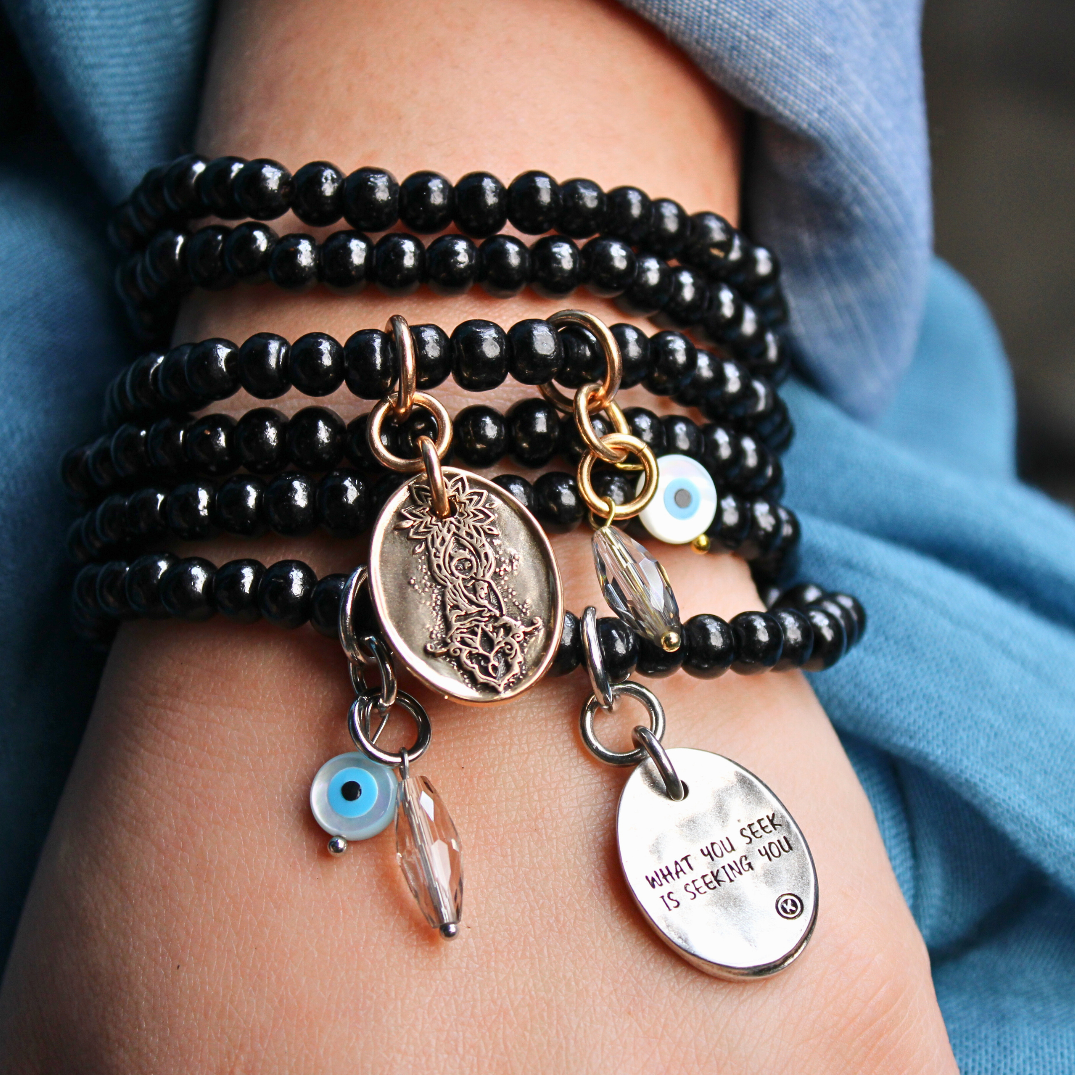 Black beaded bracelet with charms on a wrist against a blue fabric background