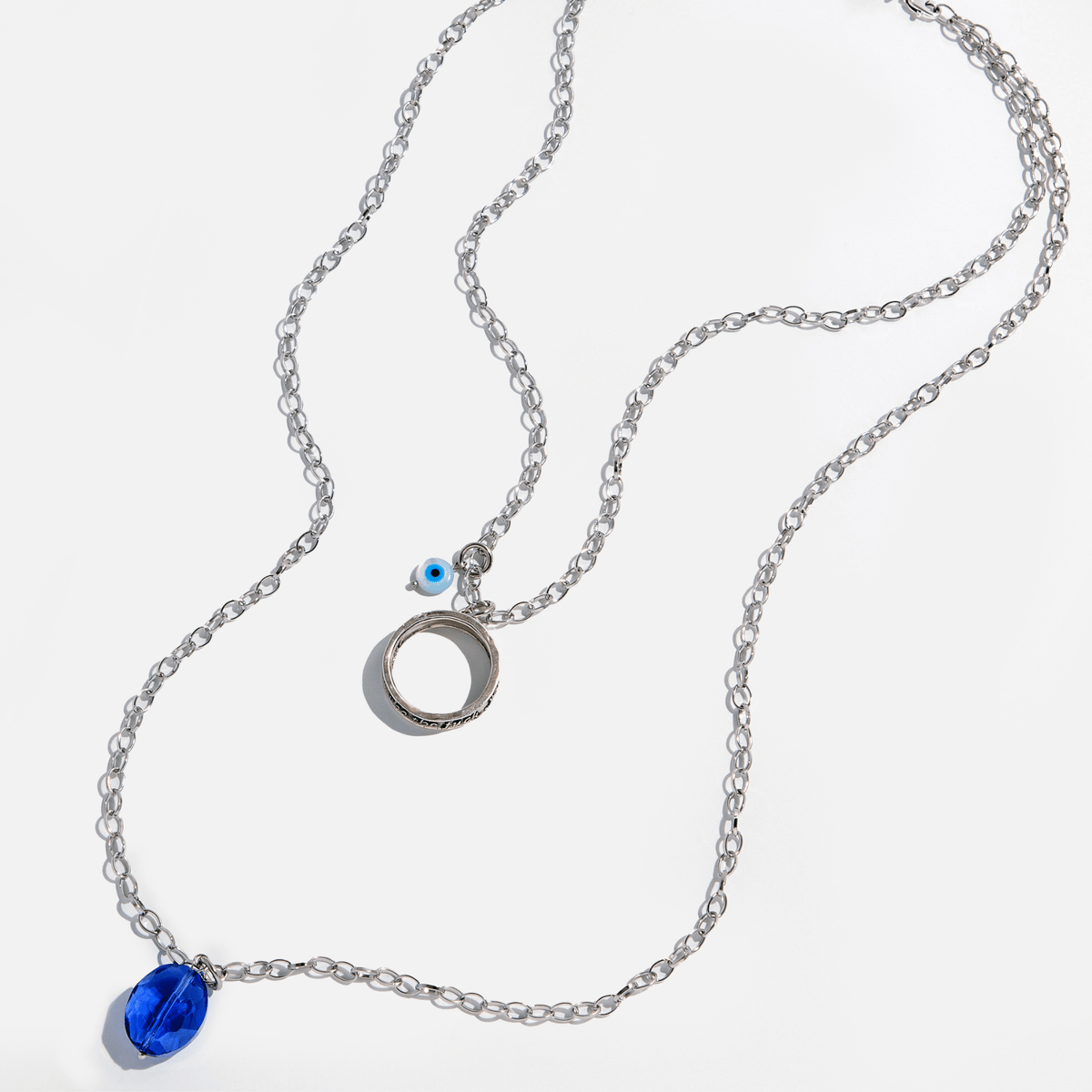 A collection of jewelry including a silver ring with an inscription, a gold necklace with a clear faceted crystal and a rose quartz heart accent, and a silver necklace with a faceted smoky crystal and moonstone accent.