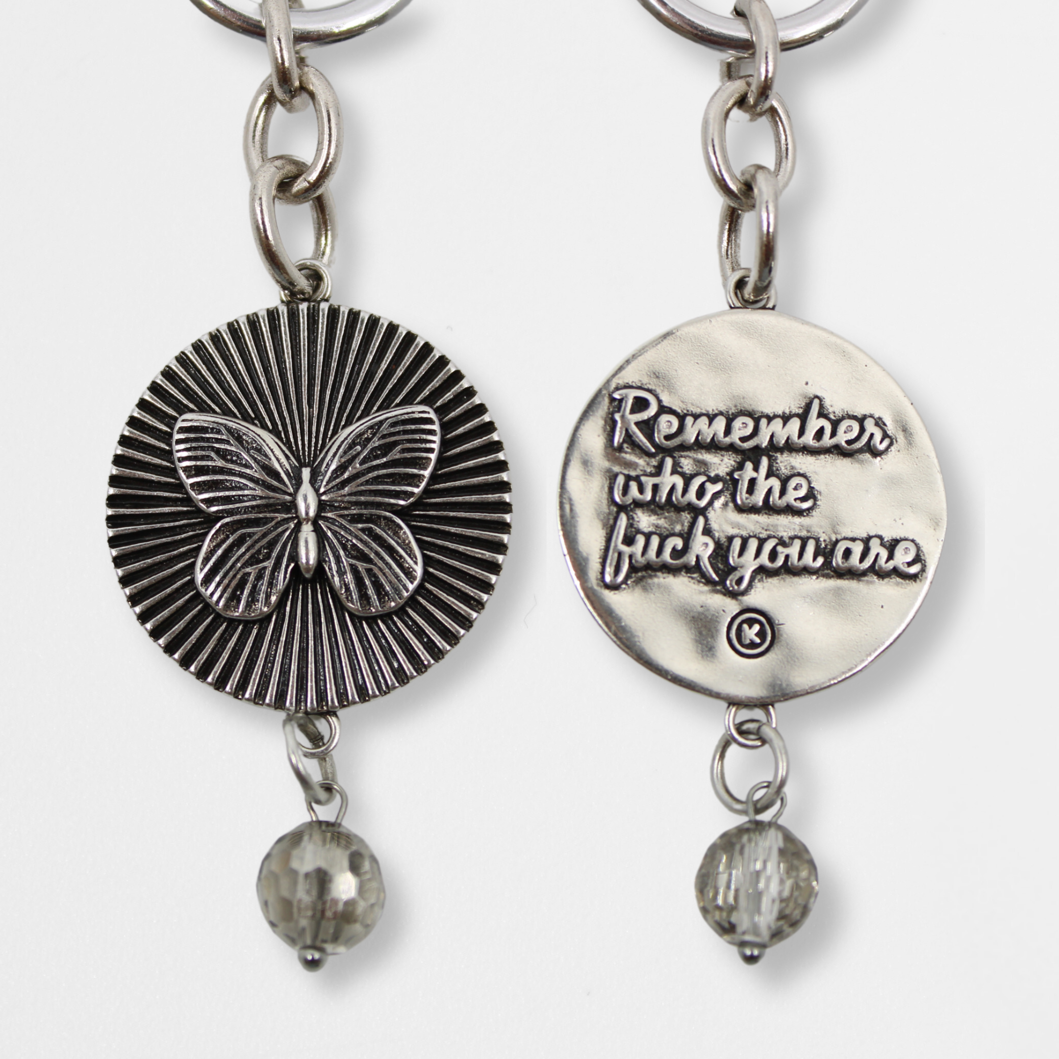 DETAILS AND PRODUCT DISPLAY OF SILVER VARIANT; one with a butterfly pendant and crystal accent, the other boldly inscribed with Remember who the fuck you are.