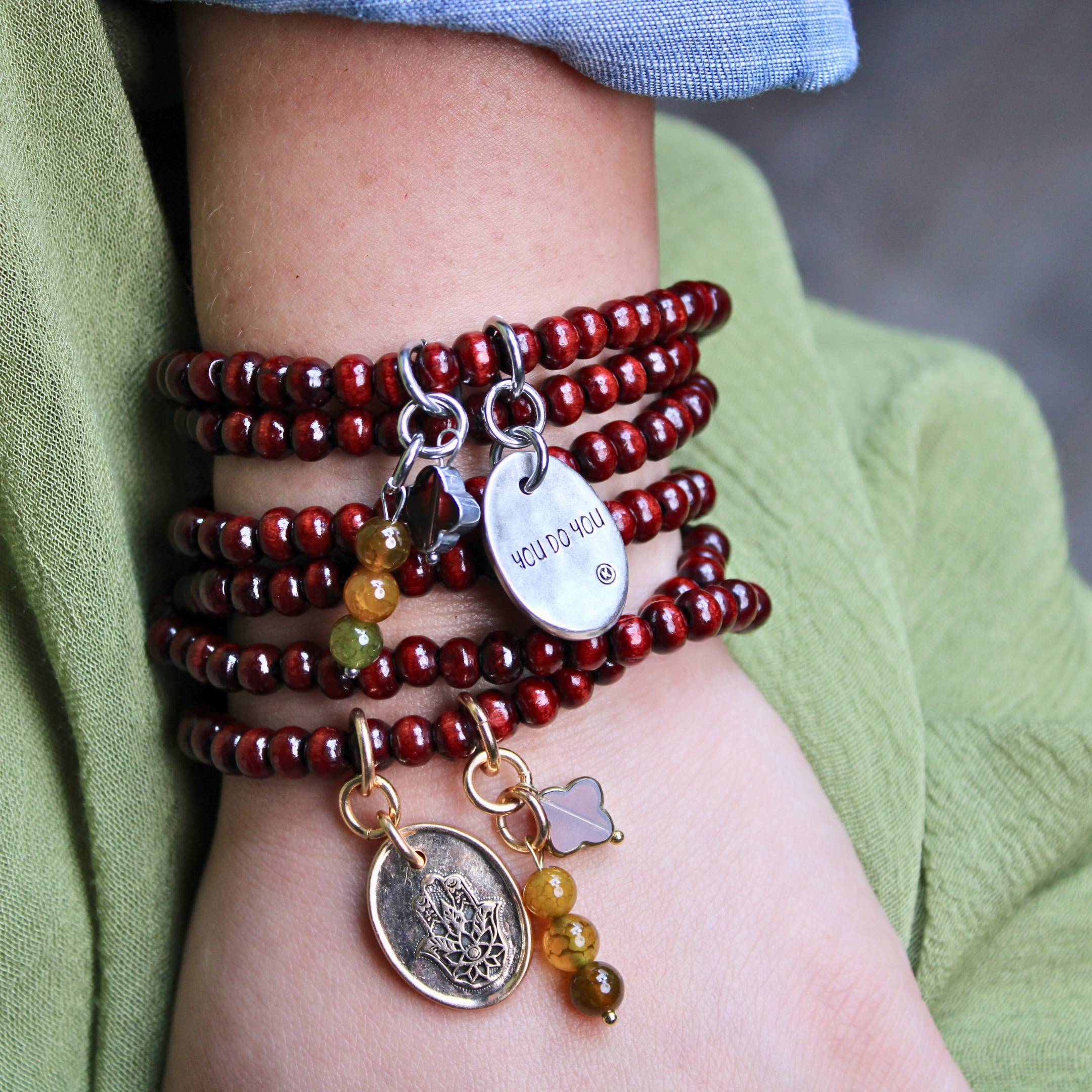 Stack of red beaded bracelets with charms on a wrist, wearing a green sleeve.
