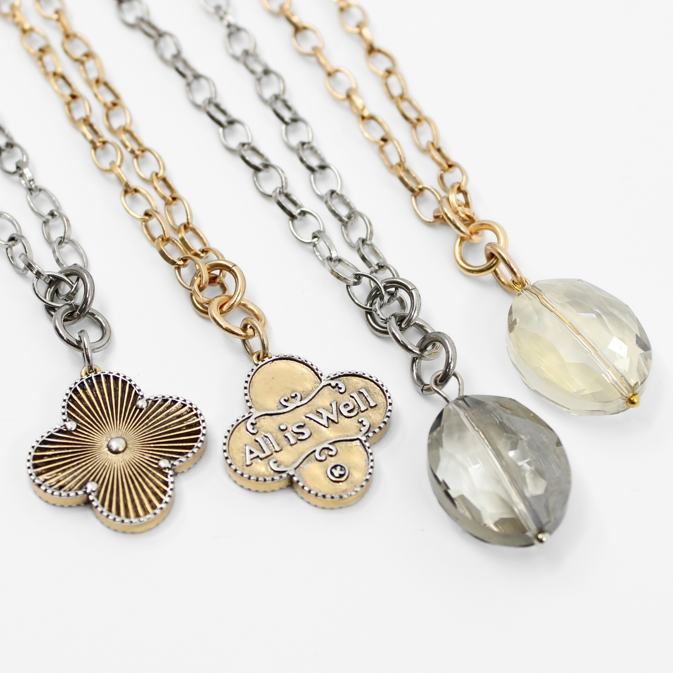 Two necklaces side by side, one with a gold chain and clover pendant, and the other with a silver chain and smoky crystal pendant.