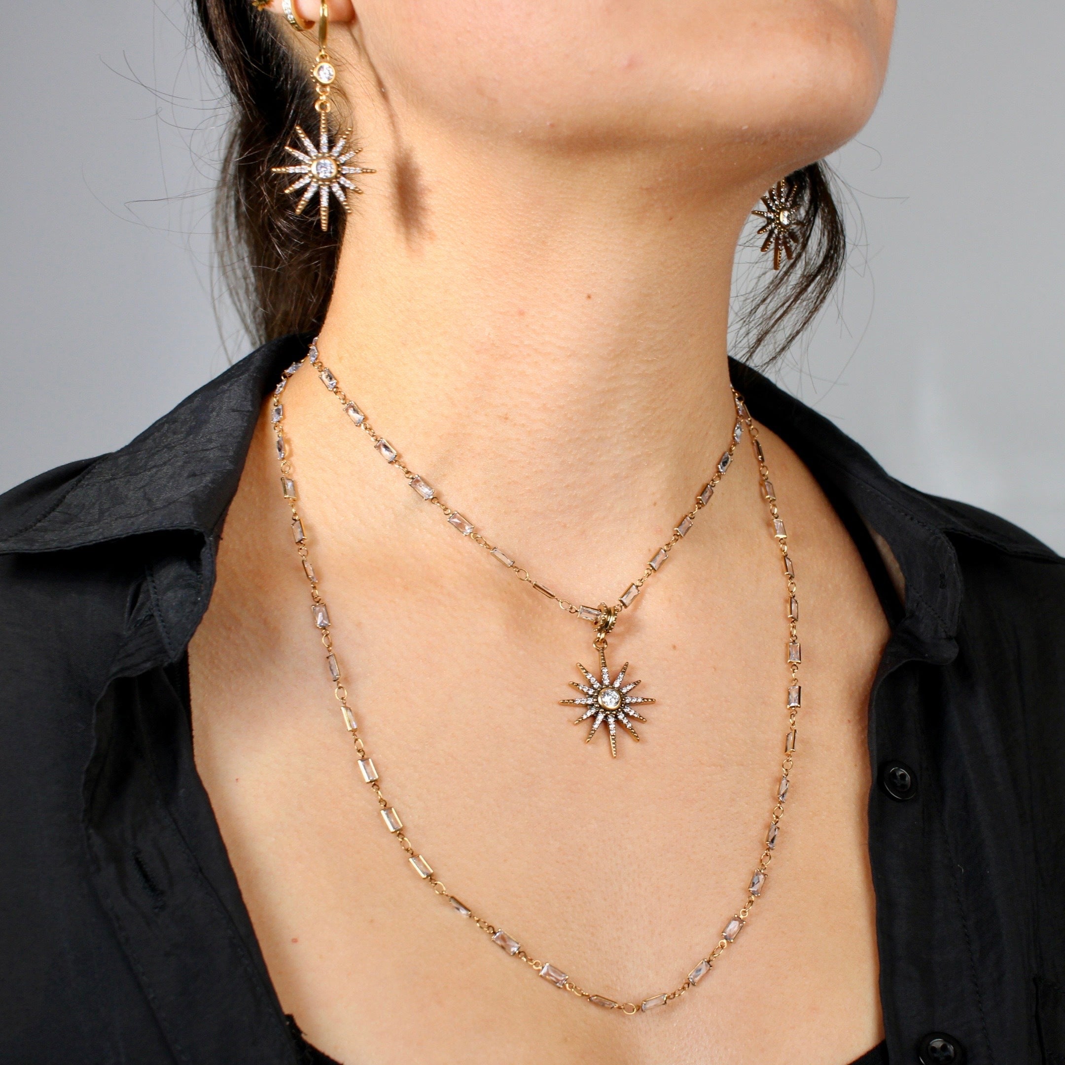 Close-up of a person wearing a gold necklace and matching earrings with a gray background