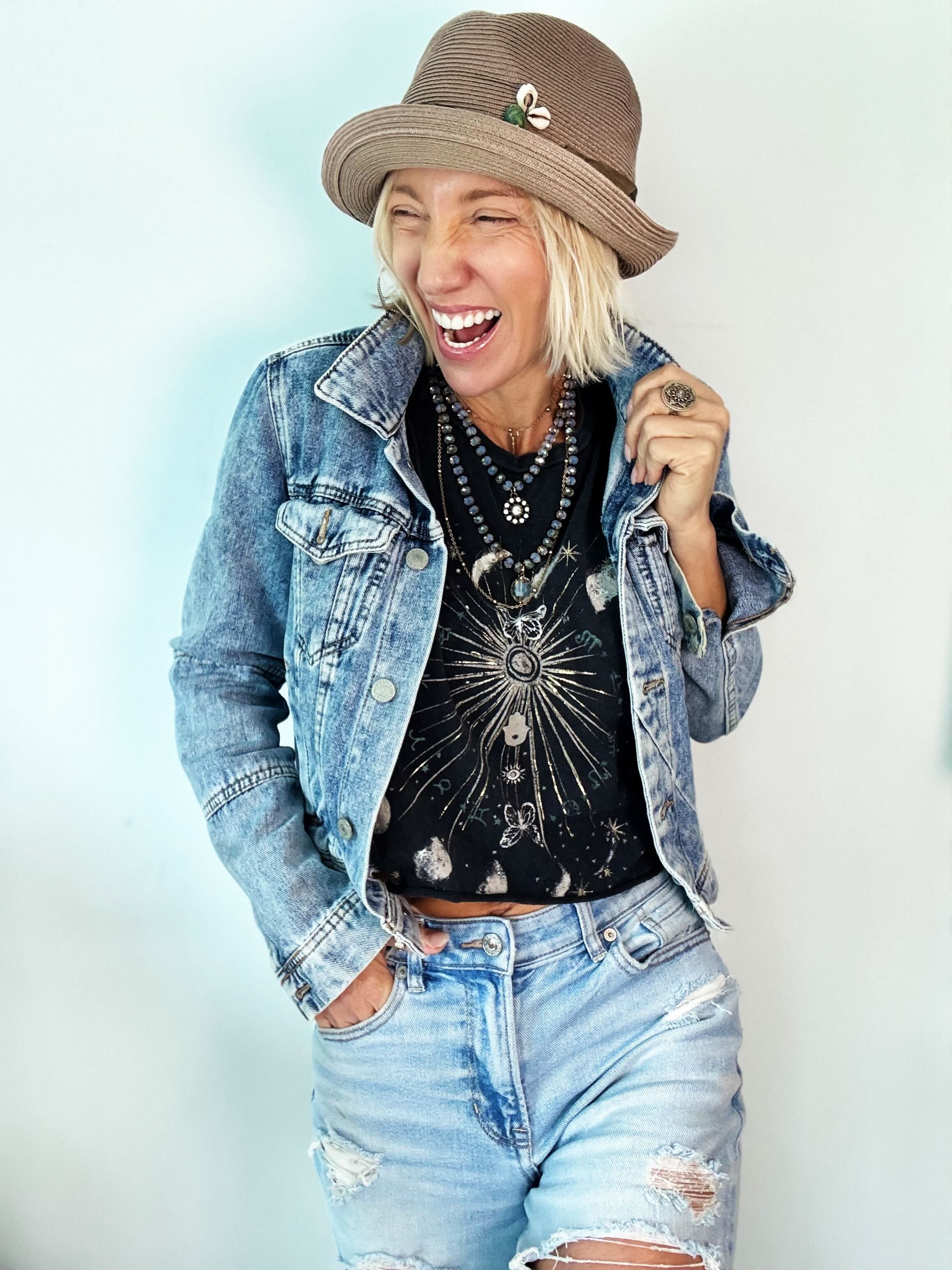 Person wearing a denim jacket, black shirt with star design, and brown hat against a light background