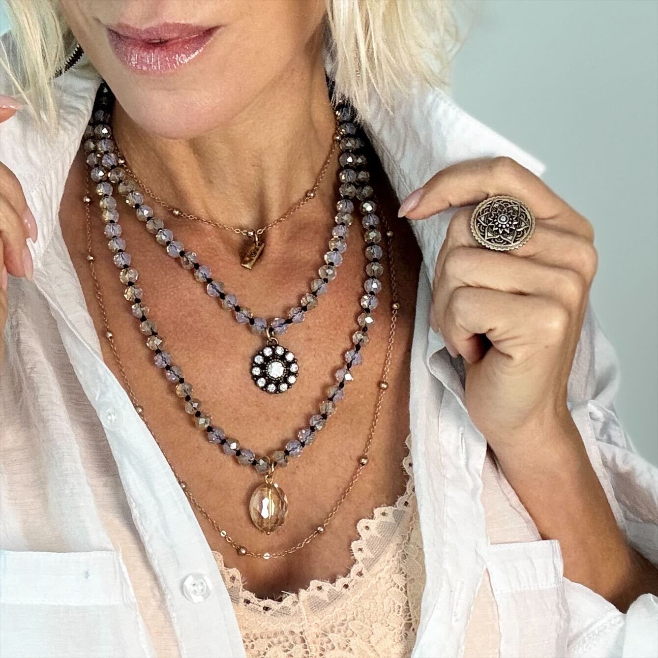 Close-up of a person wearing layered necklaces and a ring with a light background
