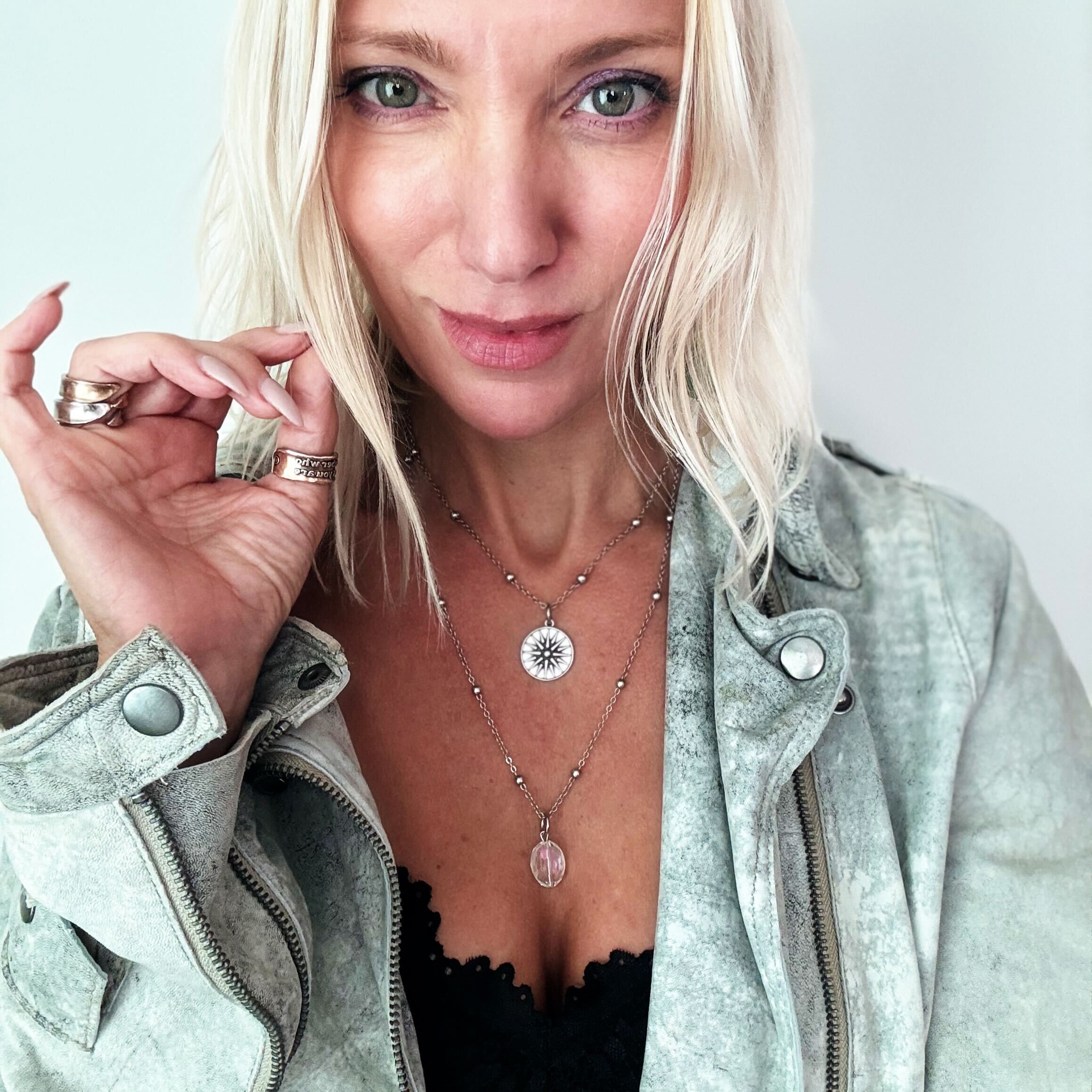 Woman wearing a light green jacket and layered necklaces with a neutral background