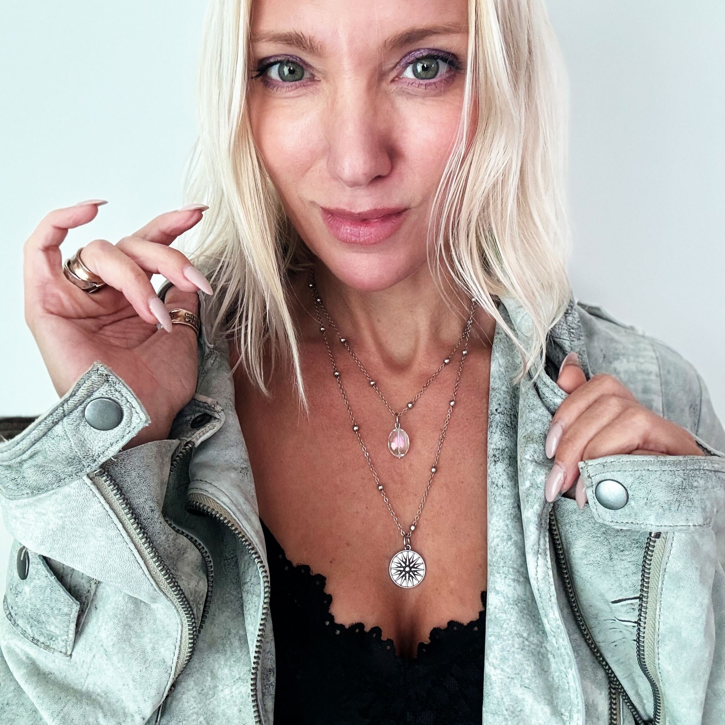 Woman wearing a light gray jacket and layered necklaces with a white background