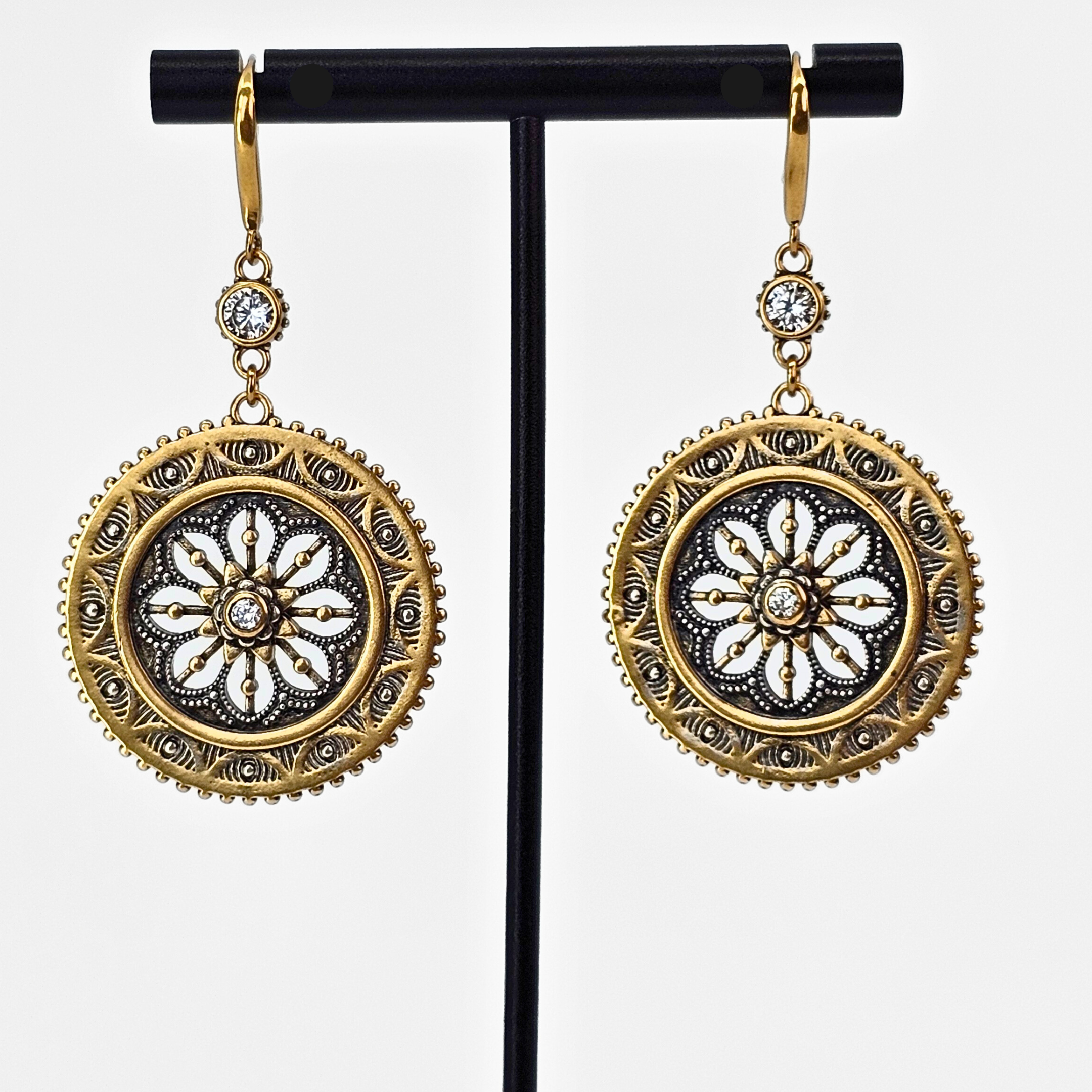 Gold and silver earrings on a black stand against a white background