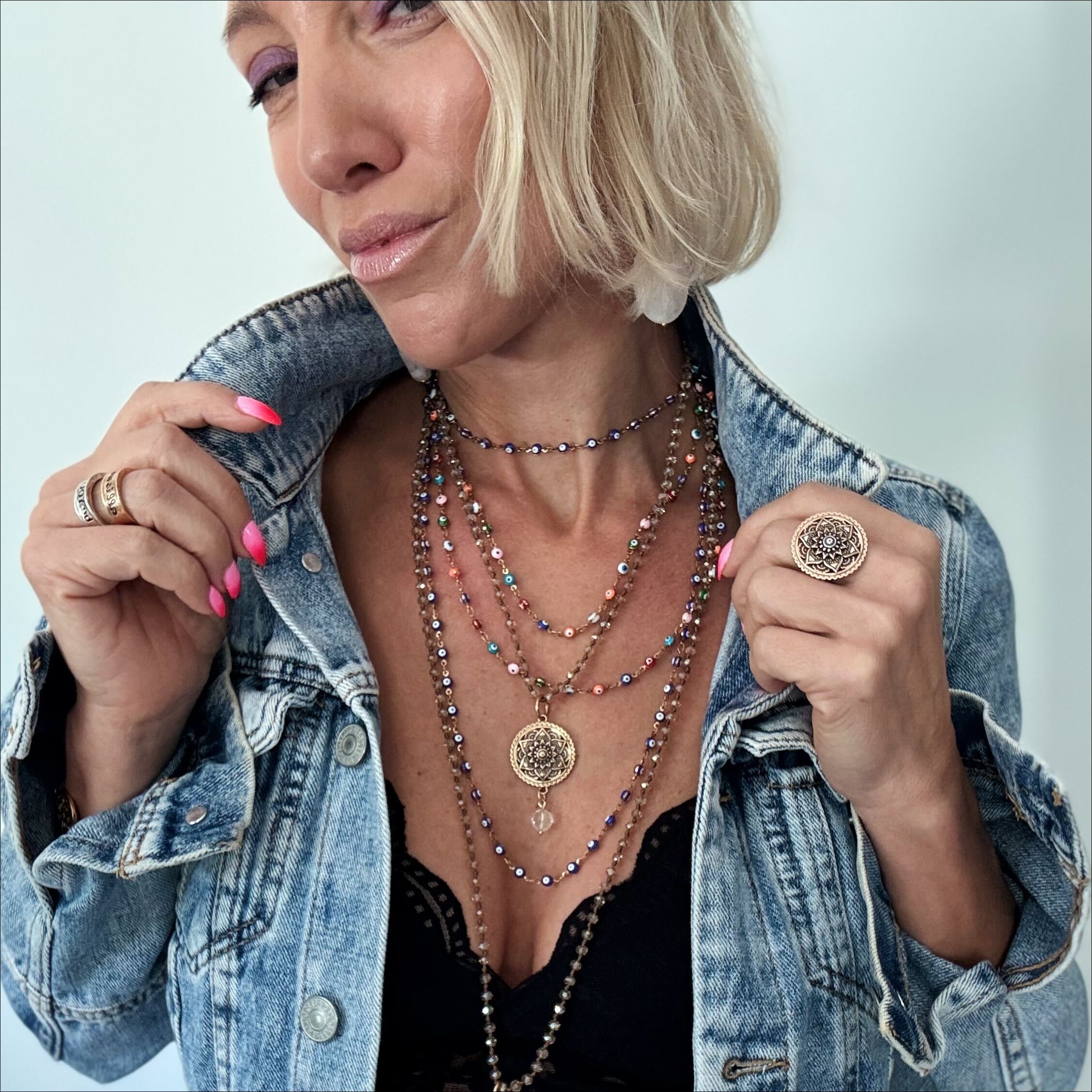 Woman wearing layered necklaces and rings with a denim jacket on a light background