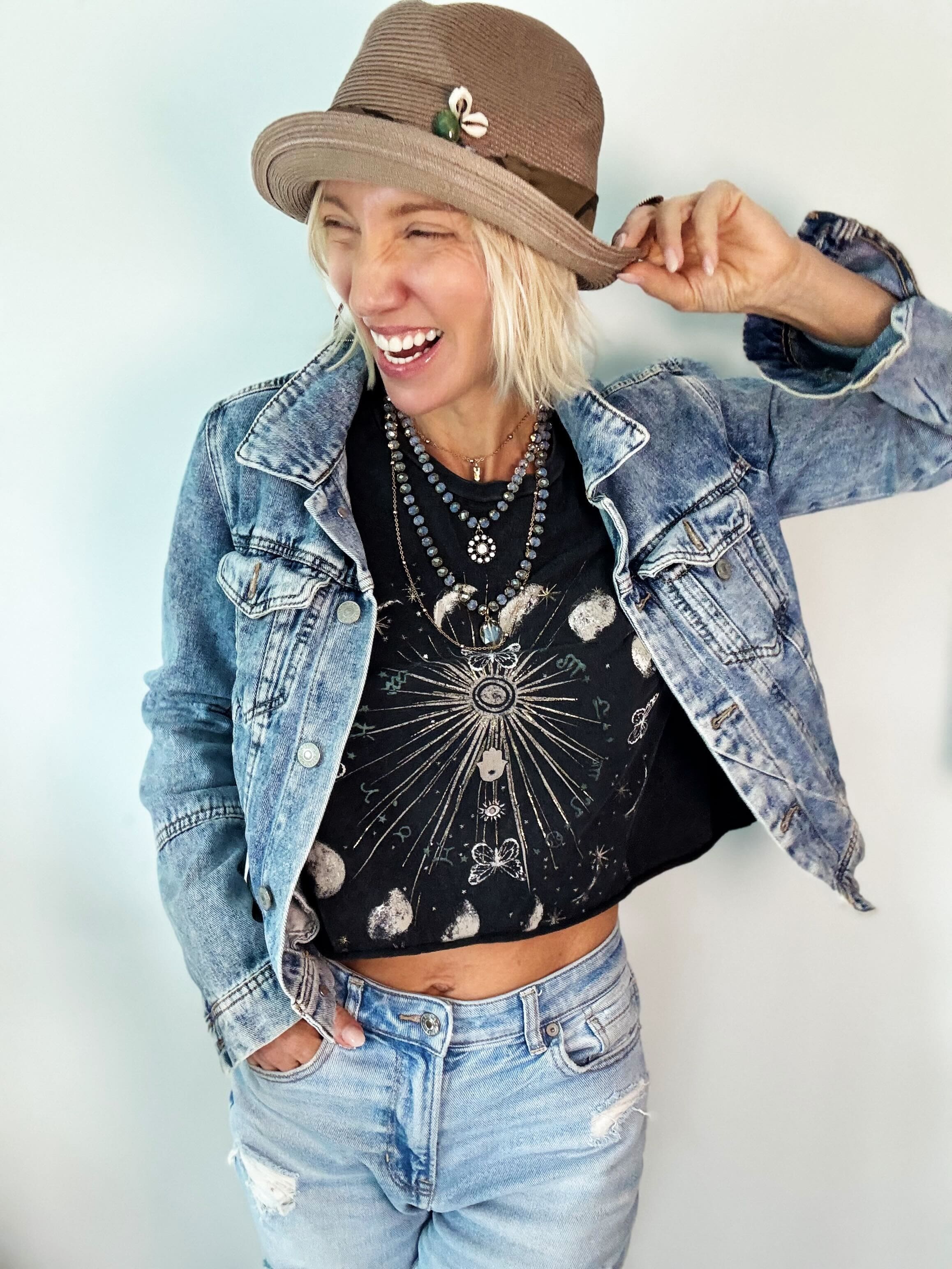 Person wearing a denim jacket, black graphic t-shirt, and brown hat against a light background