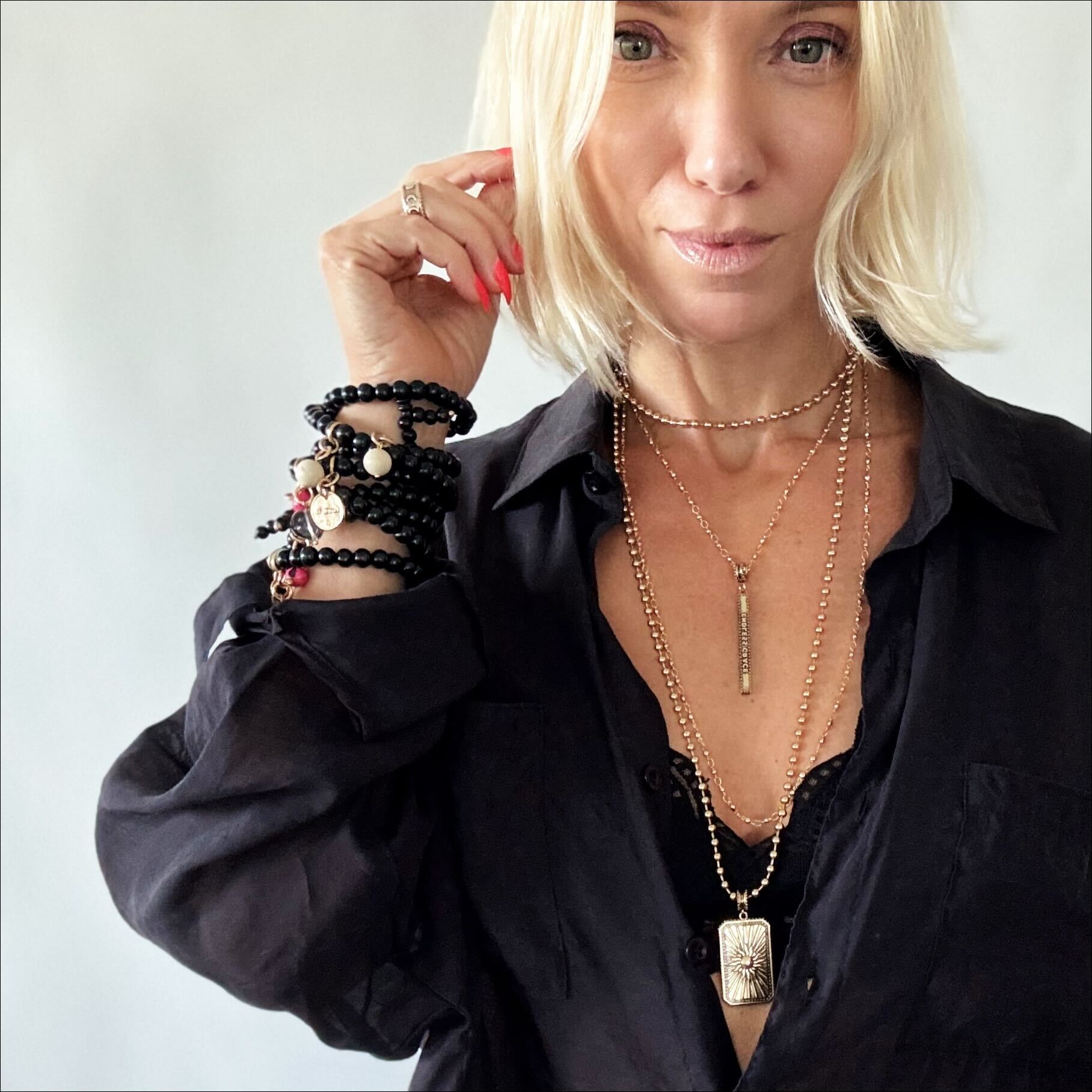 Woman wearing multiple necklaces and bracelets on a plain background