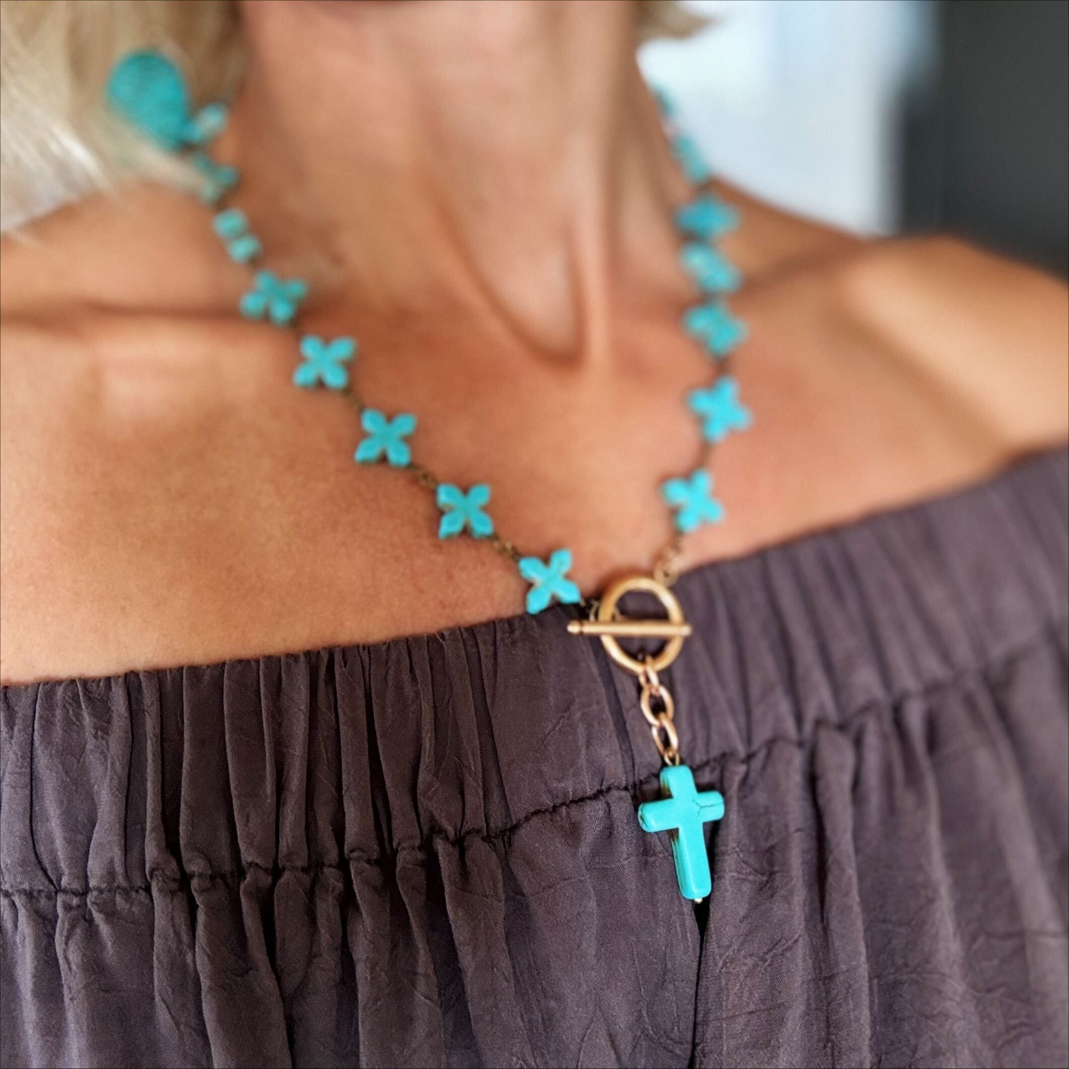 Turquoise cross necklace on a person wearing a dark gray top.