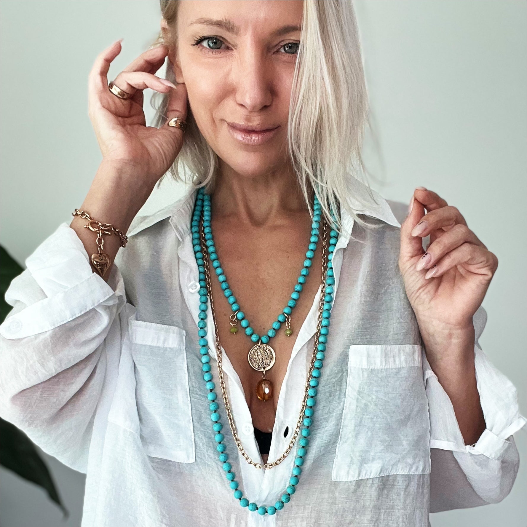 A person wearing a white shirt accessorized with a long blue howlite necklace with a chain detail and multiple pendants, along with matching bracelets.