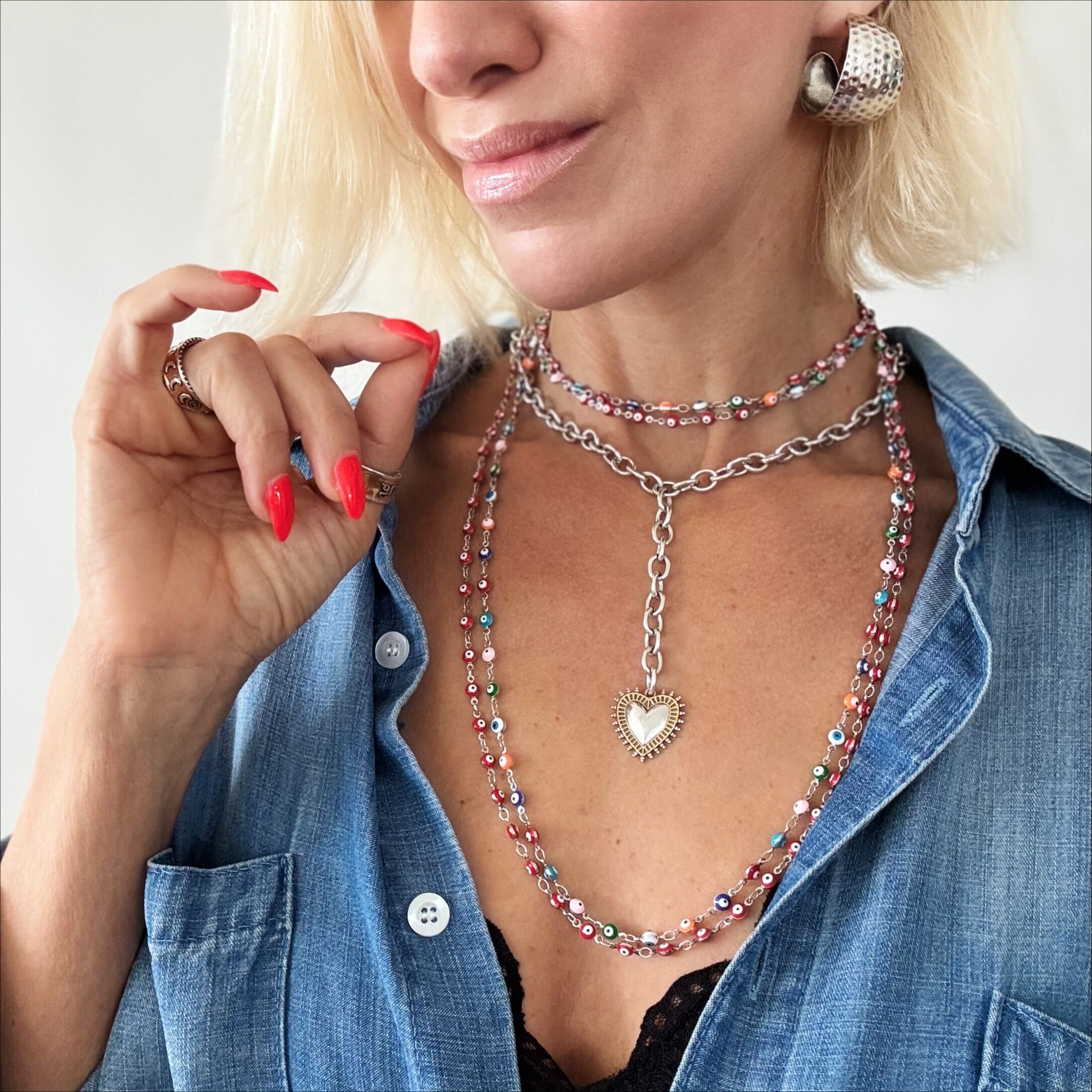 Woman wearing layered necklaces and a denim shirt with red nail polish.