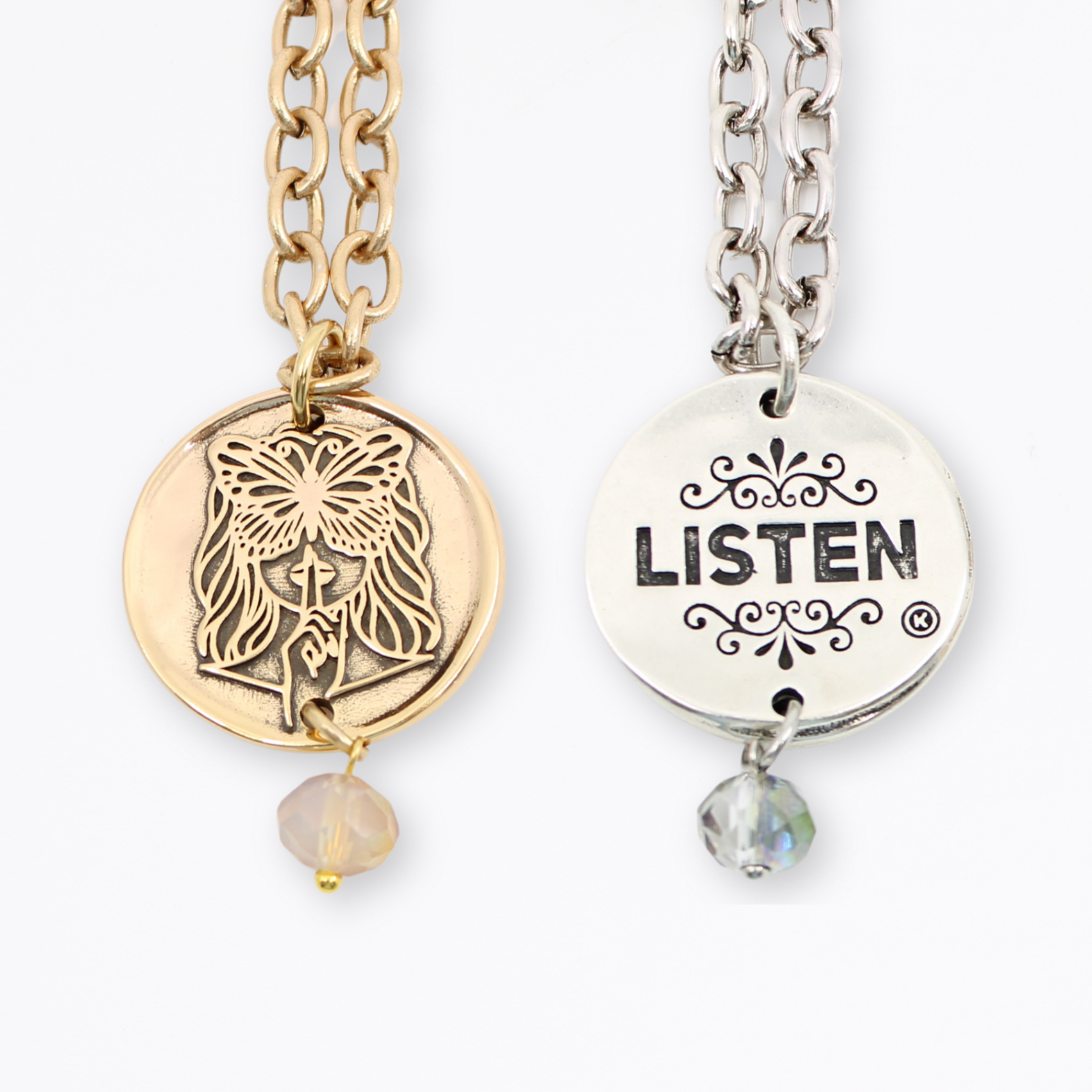 Two chain necklaces with round pendants: one silver with LISTEN adorned in plated brass and small beads, the other gold featuring a face design. Each piece exudes charm, enhanced by subtle crystal accents.
