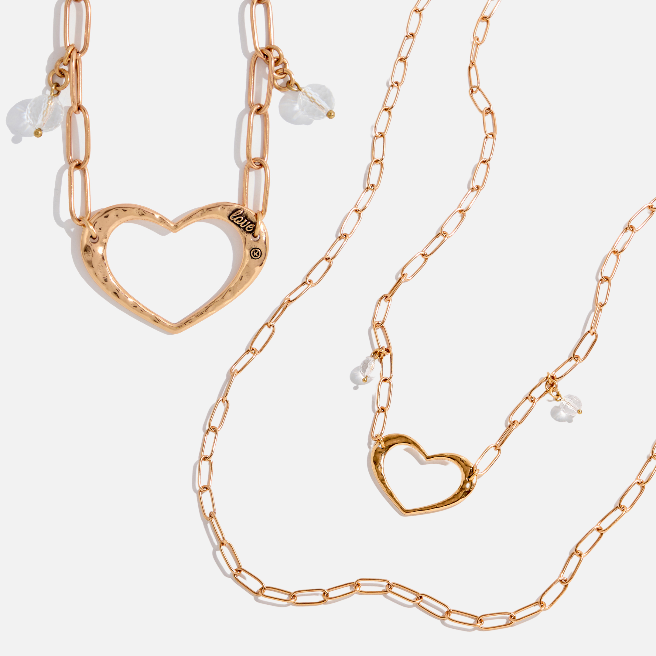 Two long chain necklaces with open heart pendants and crystal quartz accents, one with a gold-tone heart and clear quartz, and the other with a silver-tone heart and clear quartz.