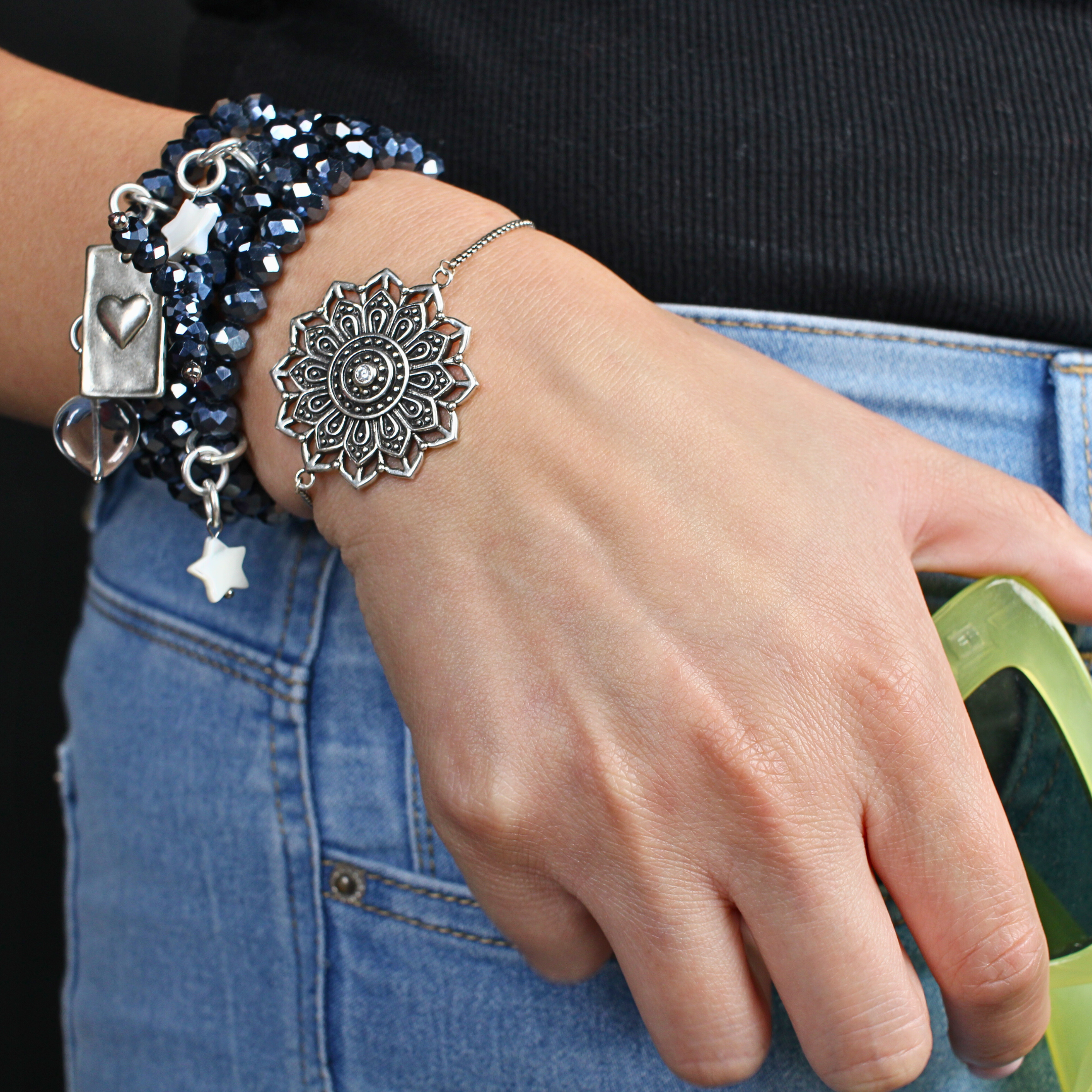 Close-up of a hand wearing multiple bracelets with decorative charms on a dark background