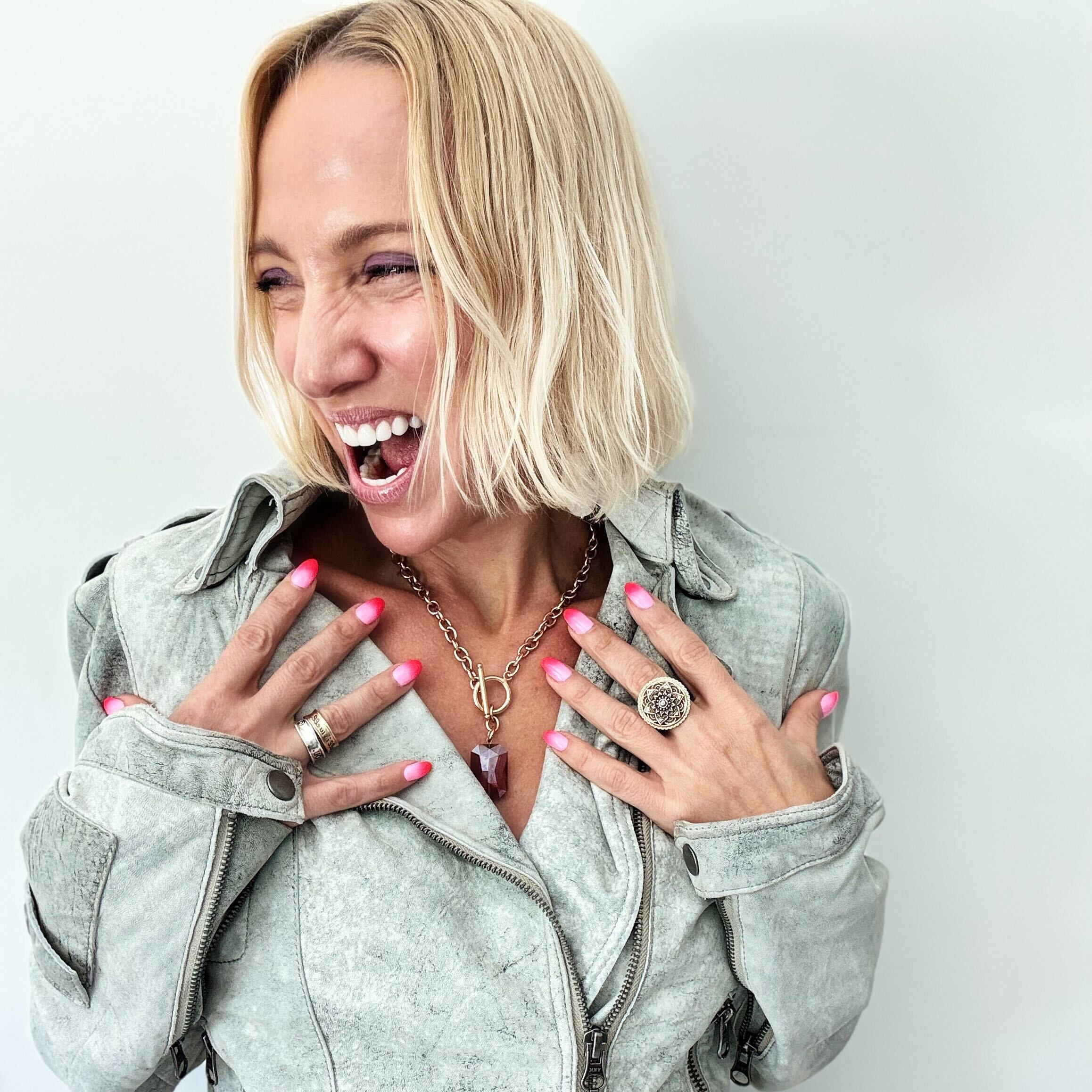 Woman wearing a light gray jacket with visible jewelry against a plain background