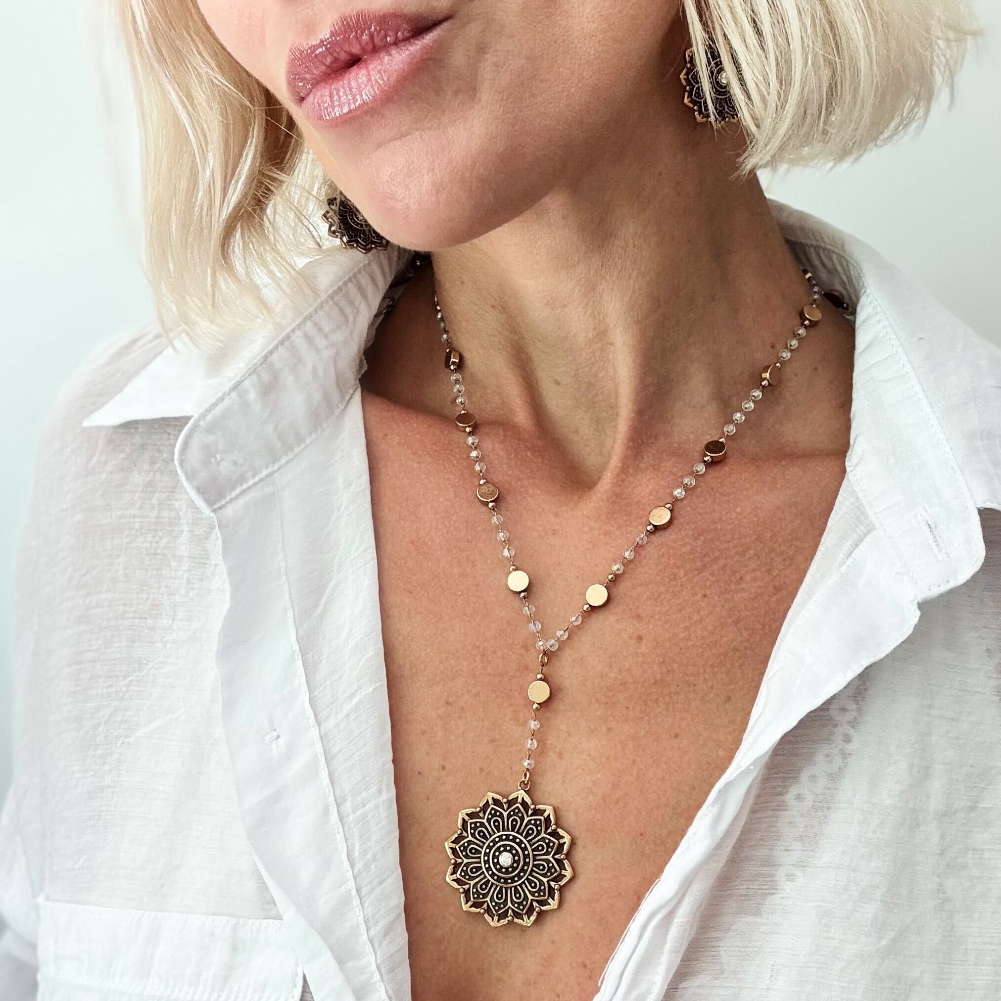 Woman wearing a long necklace with a decorative pendant against a white background