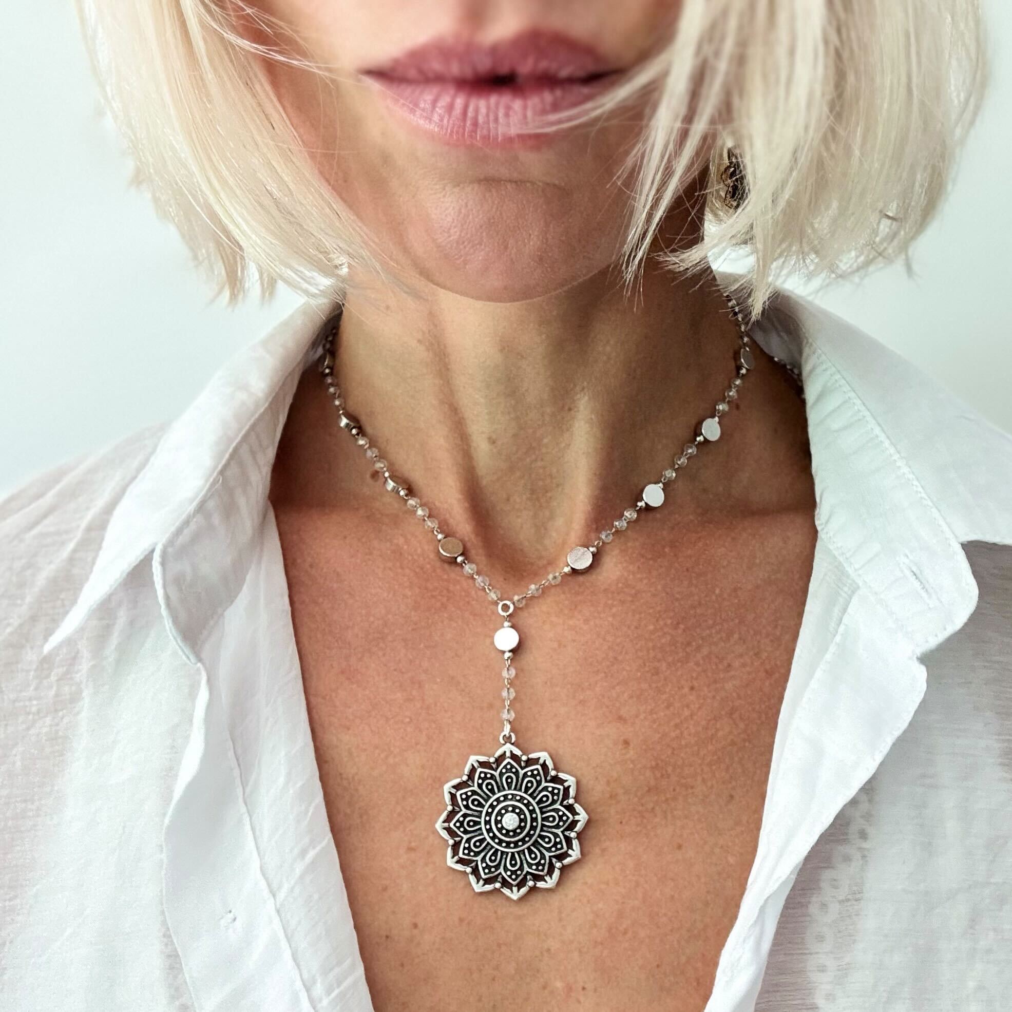 Woman wearing a silver necklace with a mandala pendant against a white background