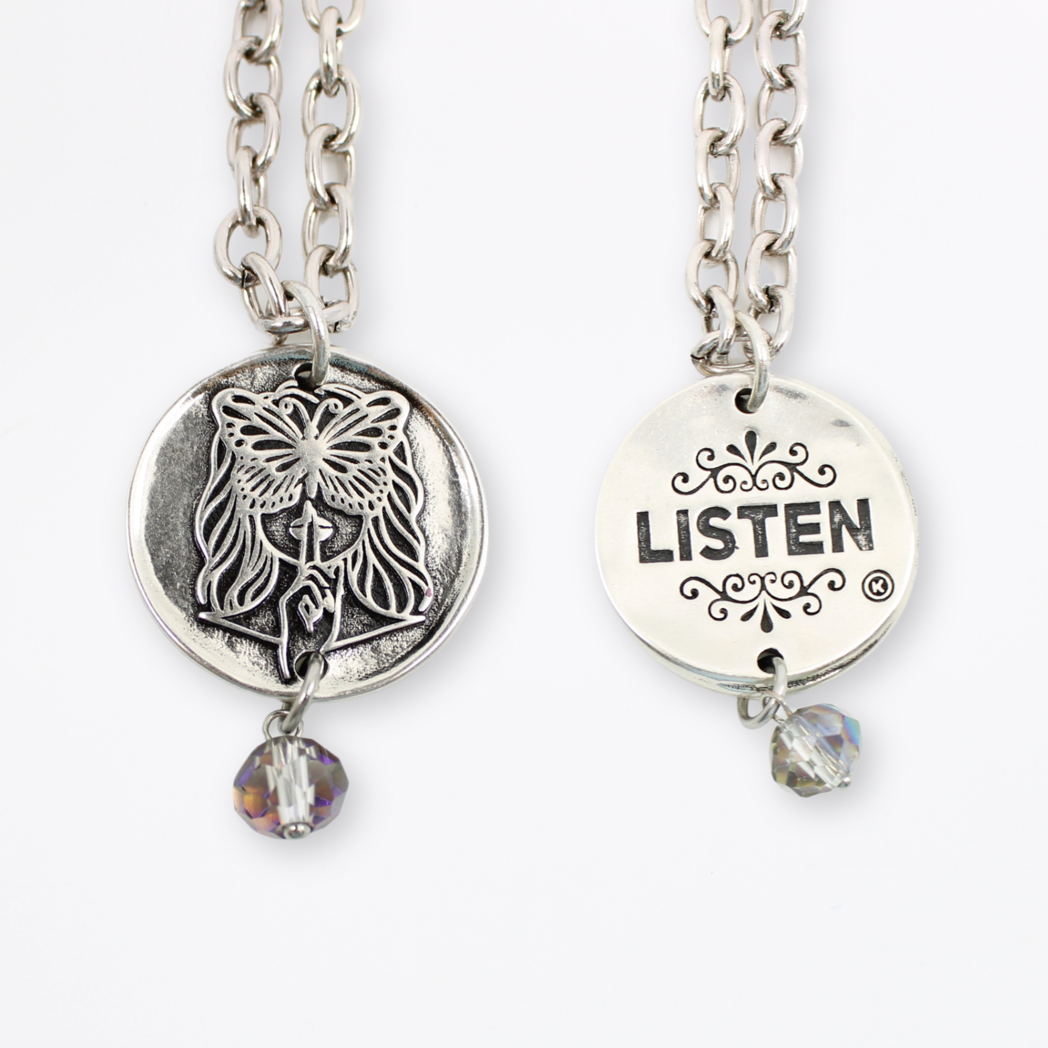 Two chain necklaces with round pendants: one silver with LISTEN adorned in plated brass and small beads, the other silver featuring a face design. Each piece exudes charm, enhanced by subtle crystal accents.